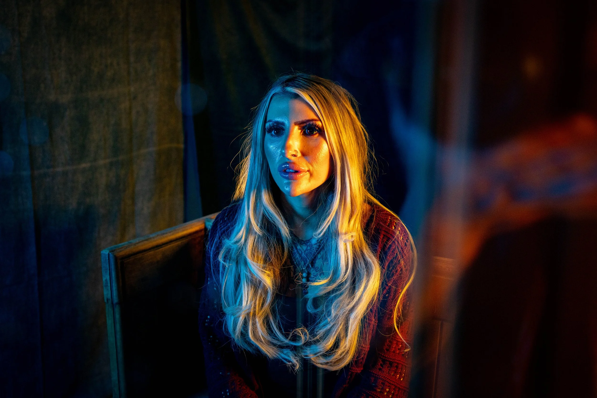 Portrait of a blonde woman with a nose ring illuminated by dramatic blue and orange lighting. Photo by Jon Rees.