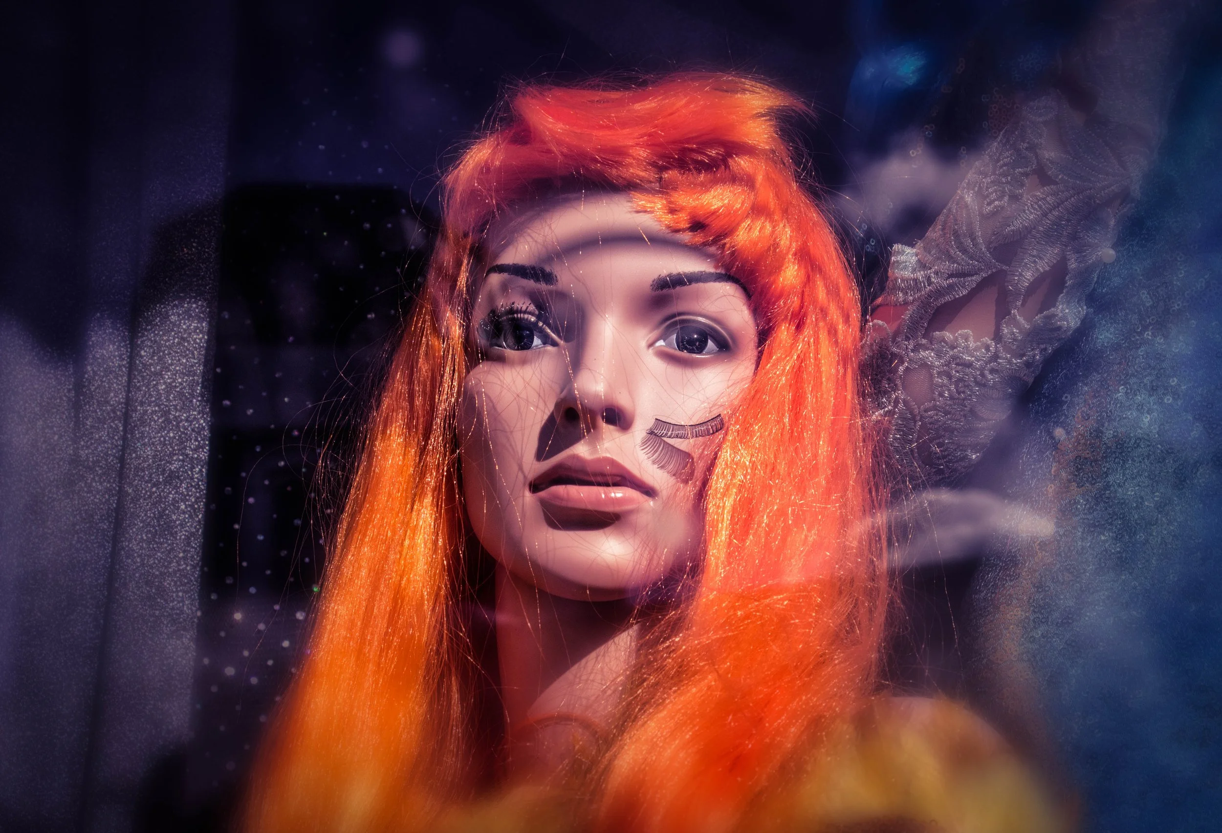 Close-up portrait of a red-haired woman with dramatic eyelashes behind a rain-speckled window. Photo by Jon Rees.