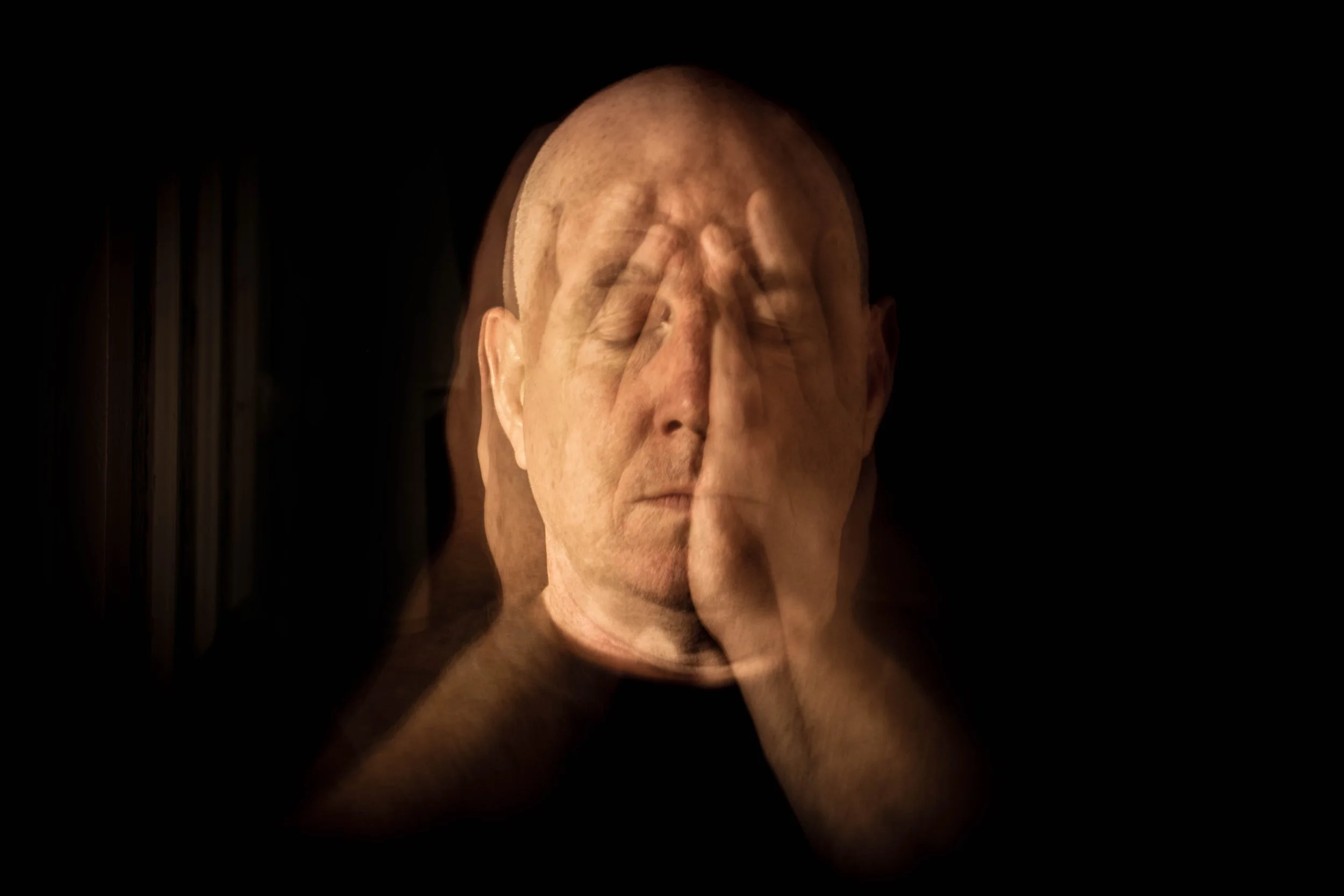 Close-up of artist Jon Rees covering his face with both hands in dim lighting. Photo by Jon Rees.