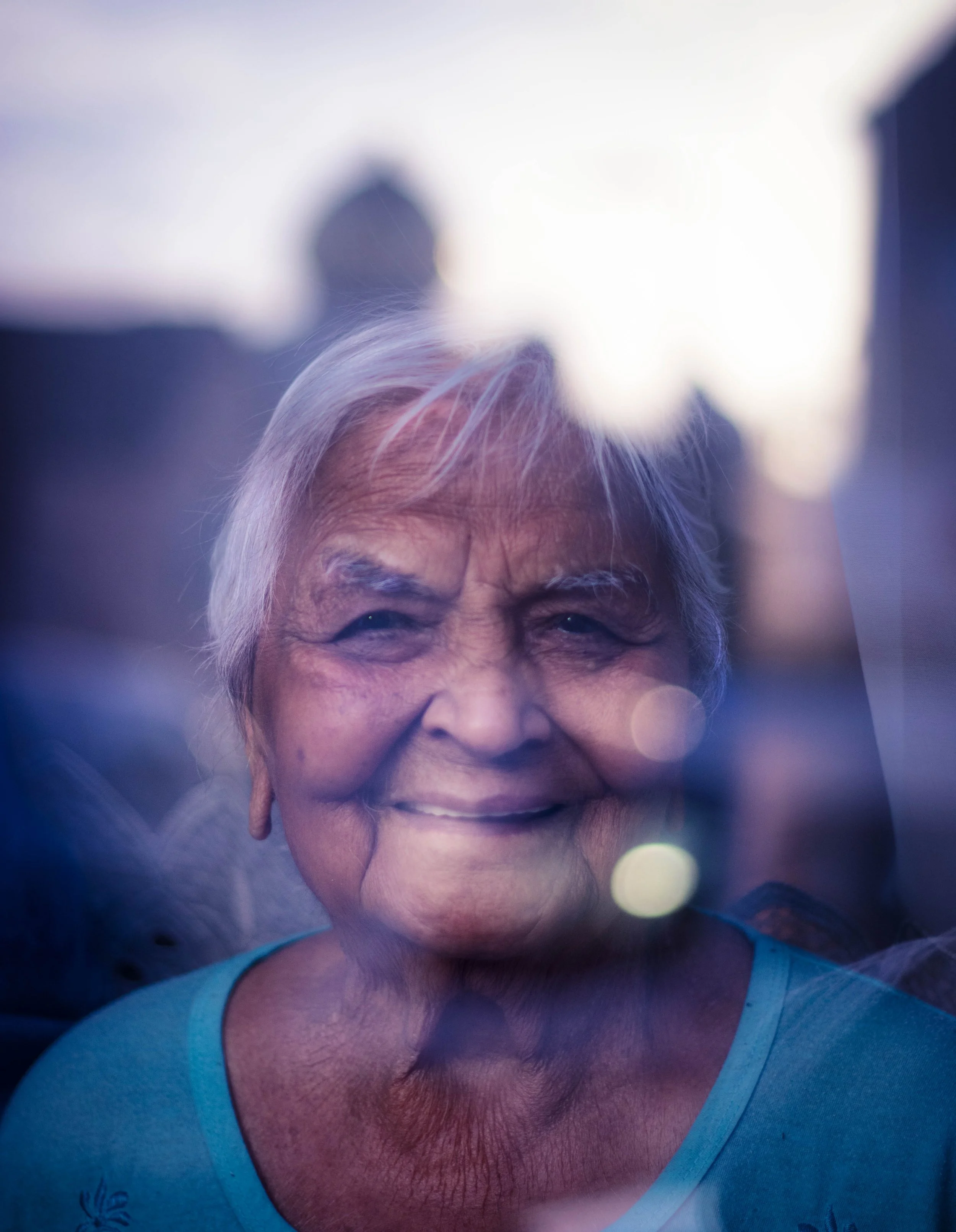 Close-up portrait of an older woman with gray hair and a gentle smile, illuminated by bright sunlight. Photo by Jon Rees.