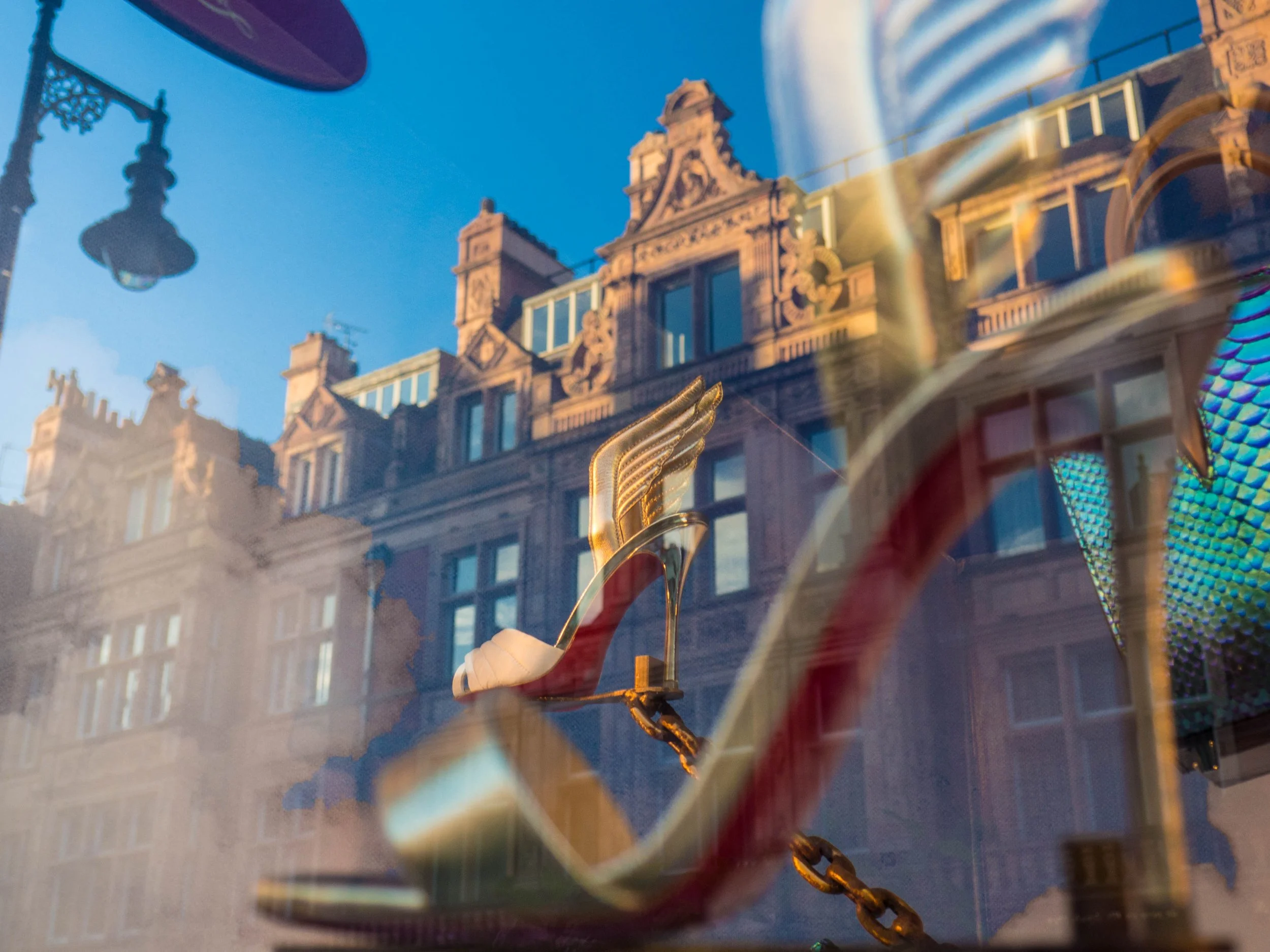 Ornate shoe store window display with a red high-heeled shoe and colorful peacock sculpture against historic European architecture. Photo by Jon Rees.