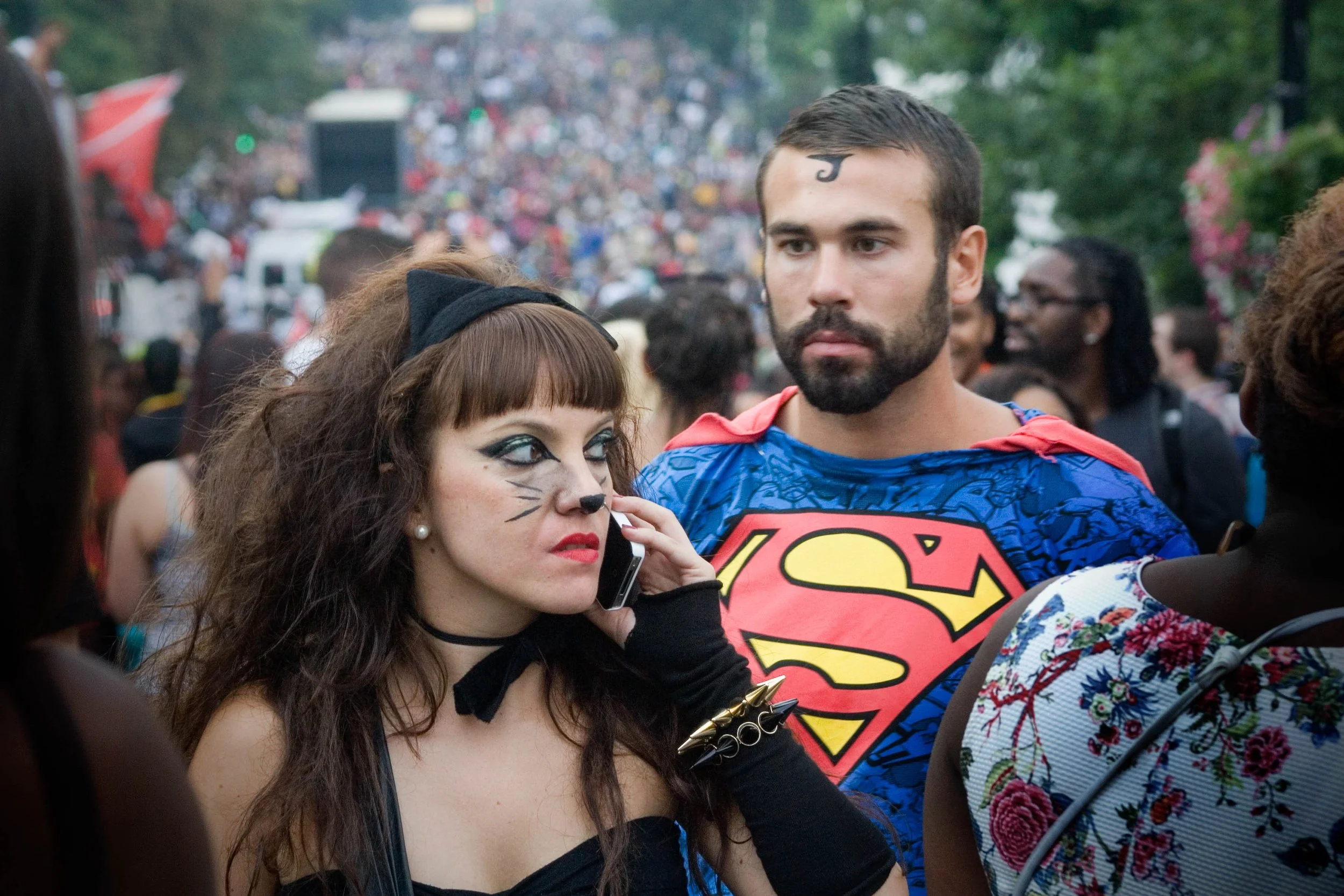 Crowded outdoor costume parade with a woman in cat makeup and a man wearing a Superman costume. Photo by Jon Rees.