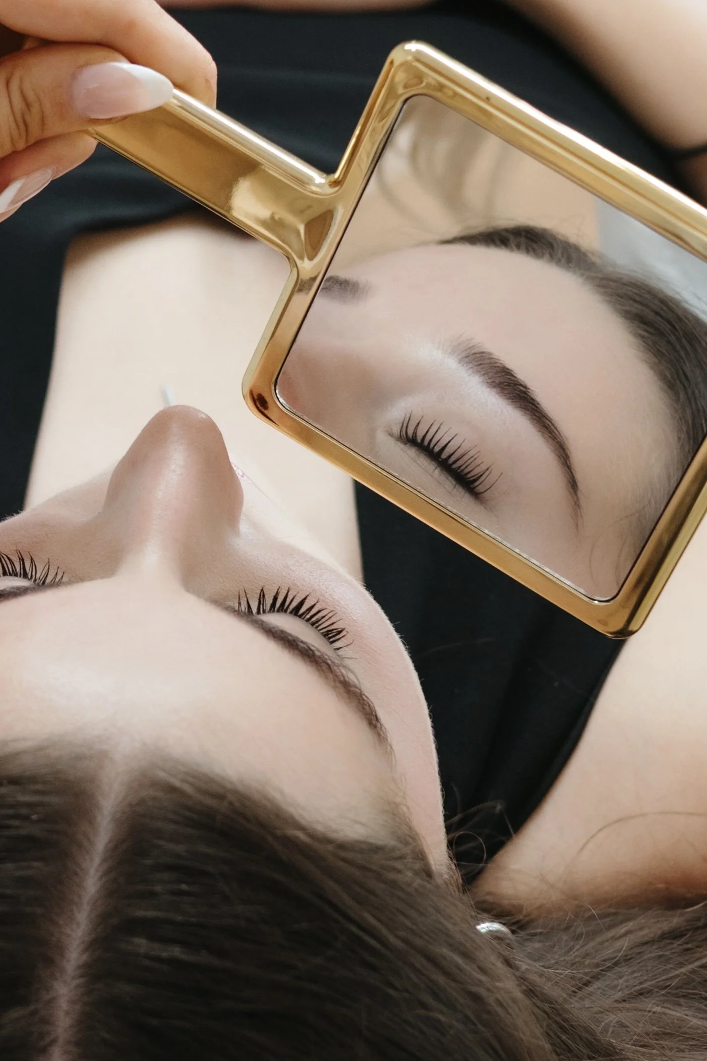Client holding a gold mirror showing a close-up of her lashes and brows.