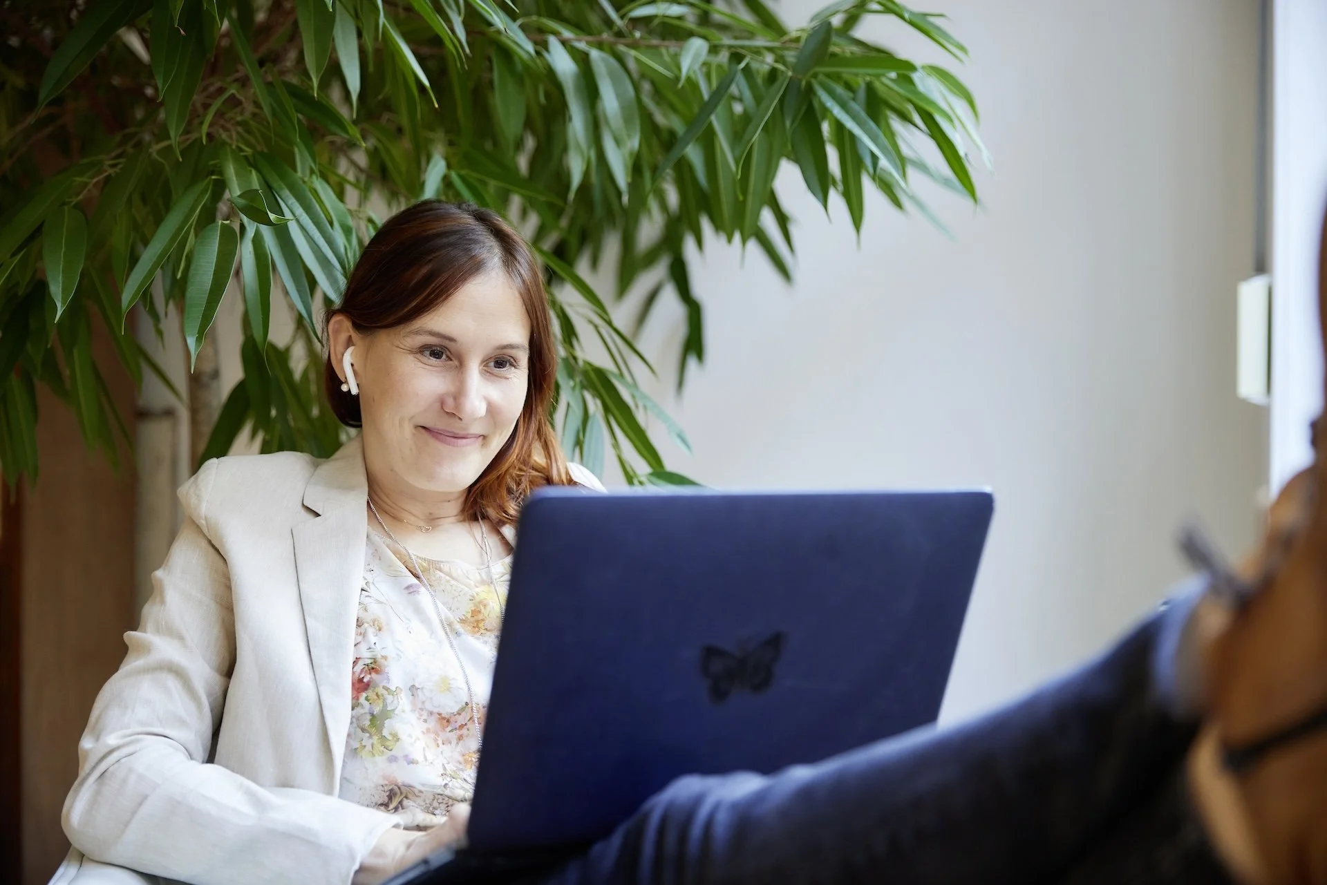 Andrea using her laptop indoors in her private practice, with a large green plant in the background
