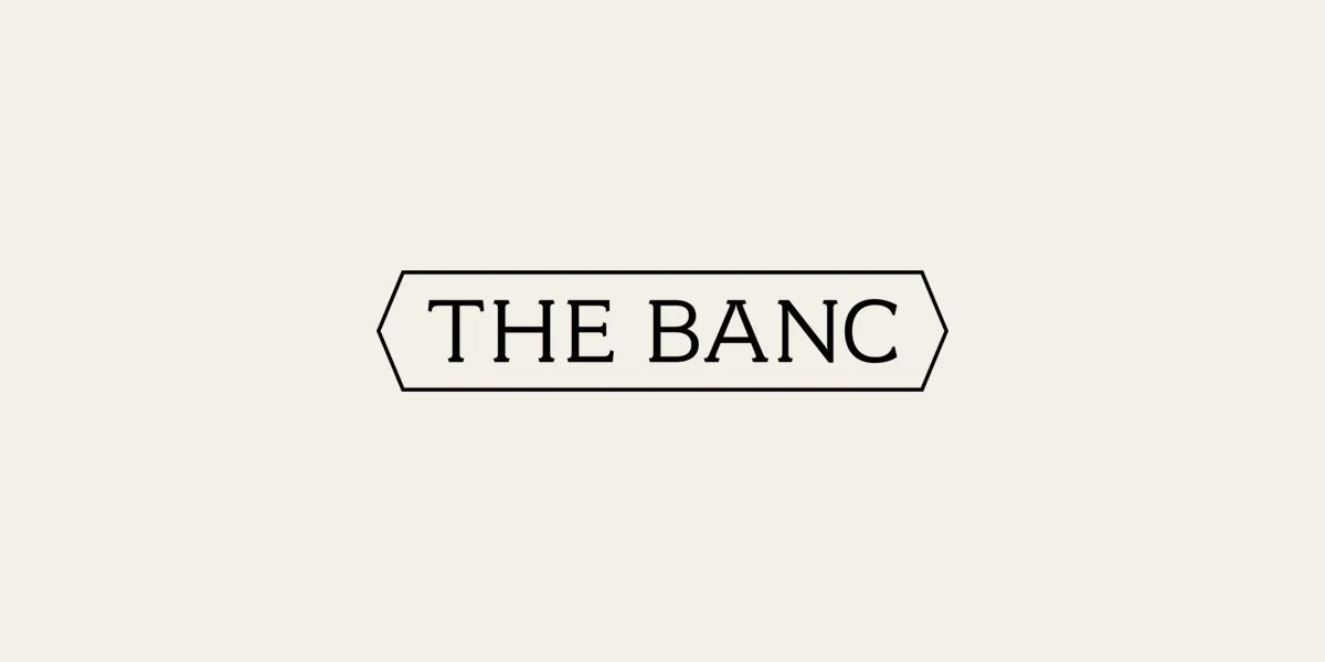 Minimalist black outlined sign reading “THE BANC” on an off-white background