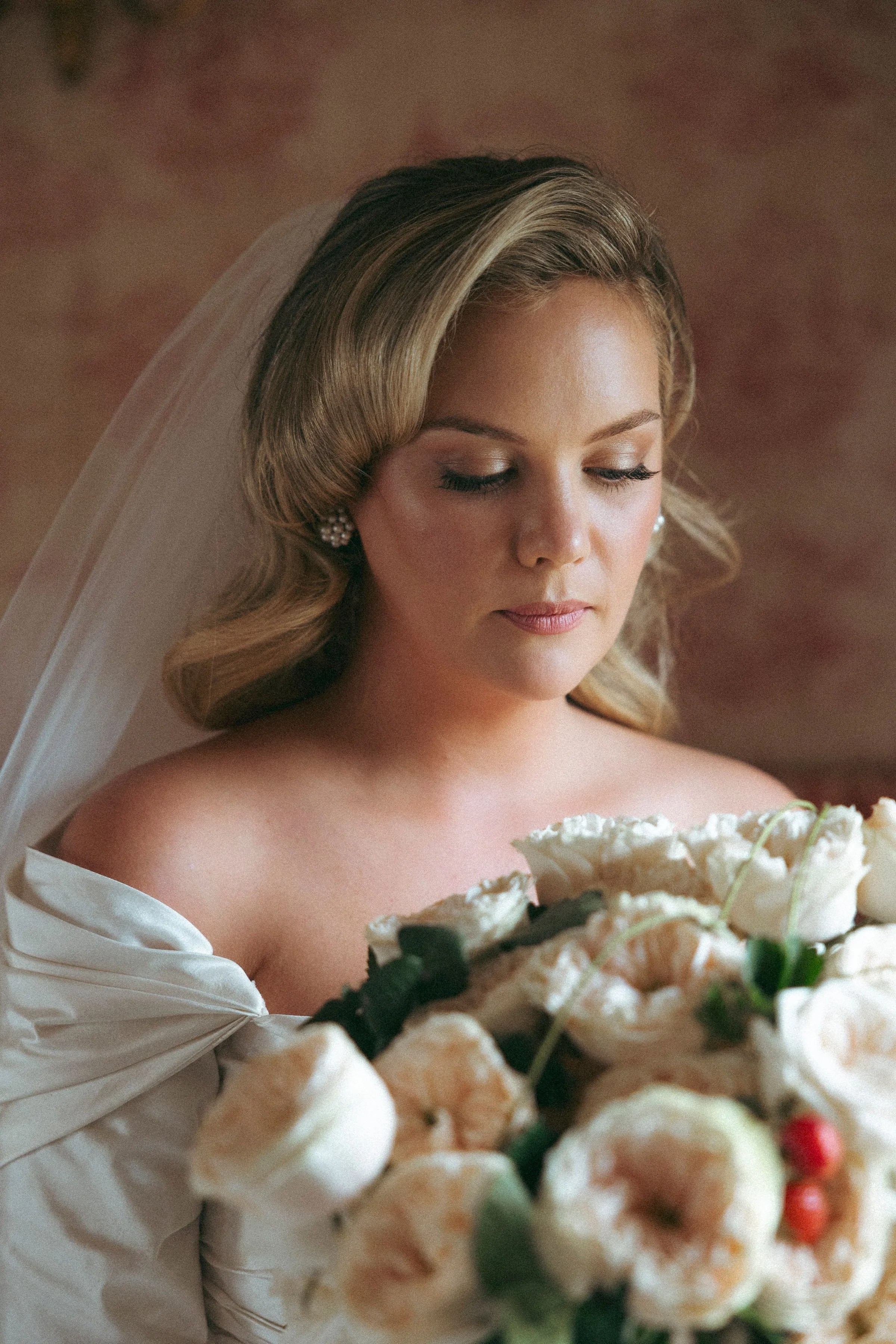Close-up portrait of a bride with closed eyes, wearing a veil and holding a bouquet of white flowers