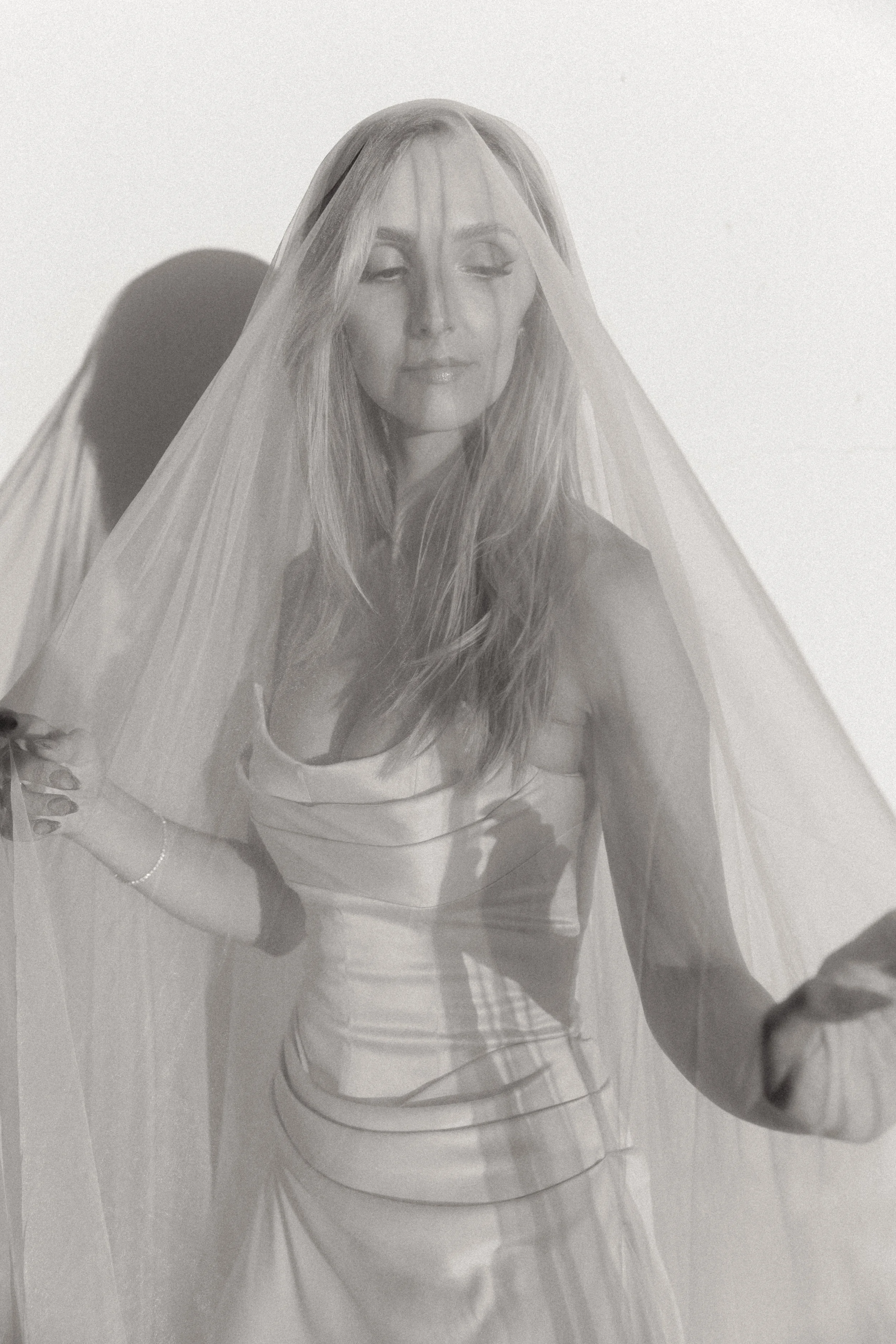 Black-and-white portrait of a smiling woman wearing a bridal veil and holding a bouquet.