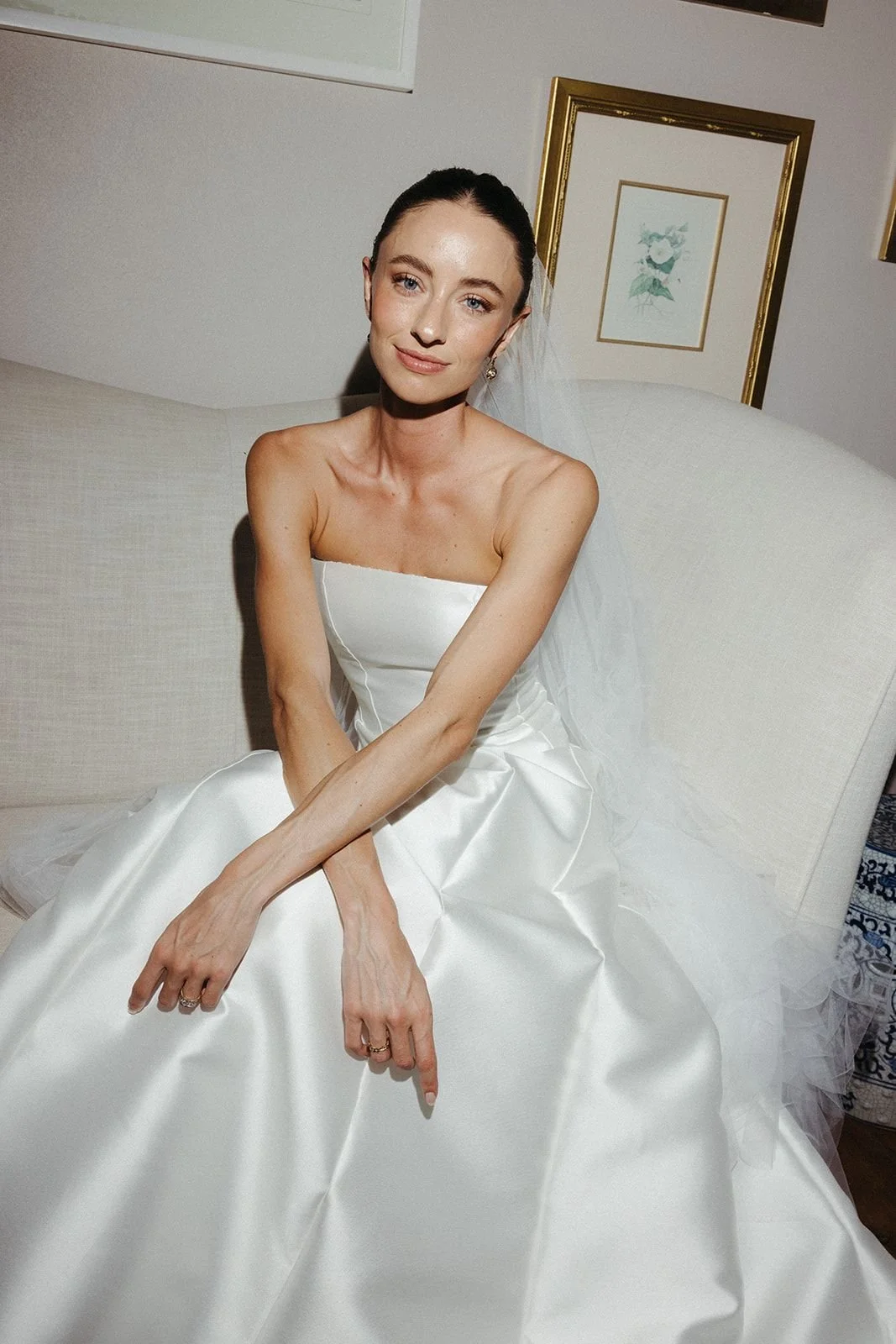 Bride in a strapless white wedding gown and veil sitting on a white sofa
