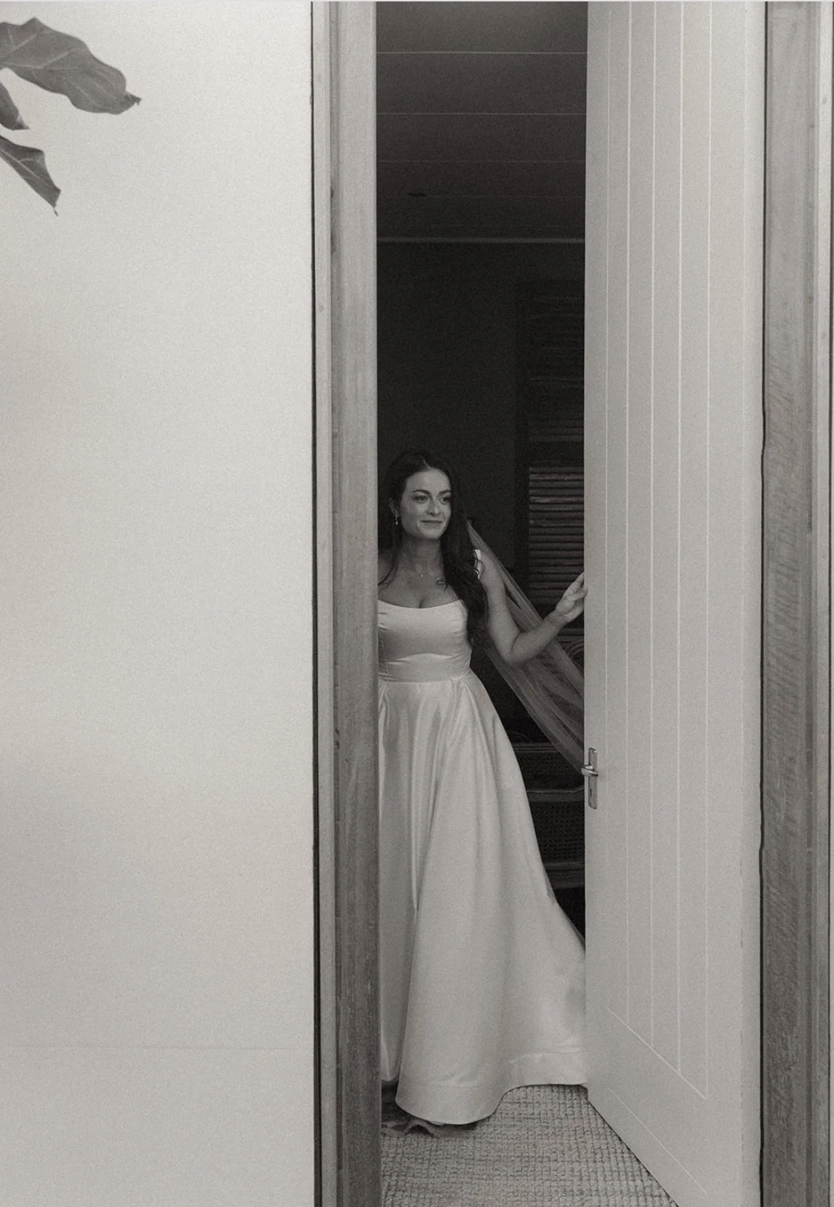 Black-and-white portrait of a woman in a long flowing dress standing in a doorway