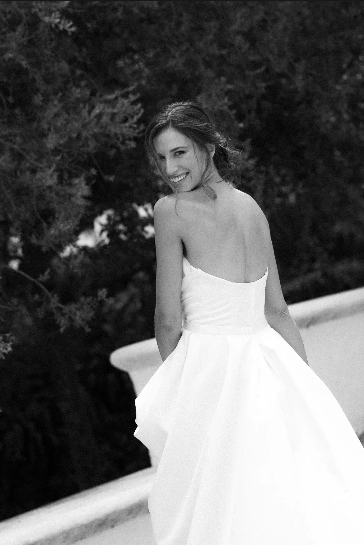 Smiling woman in a strapless white wedding dress posing outdoors in black and white