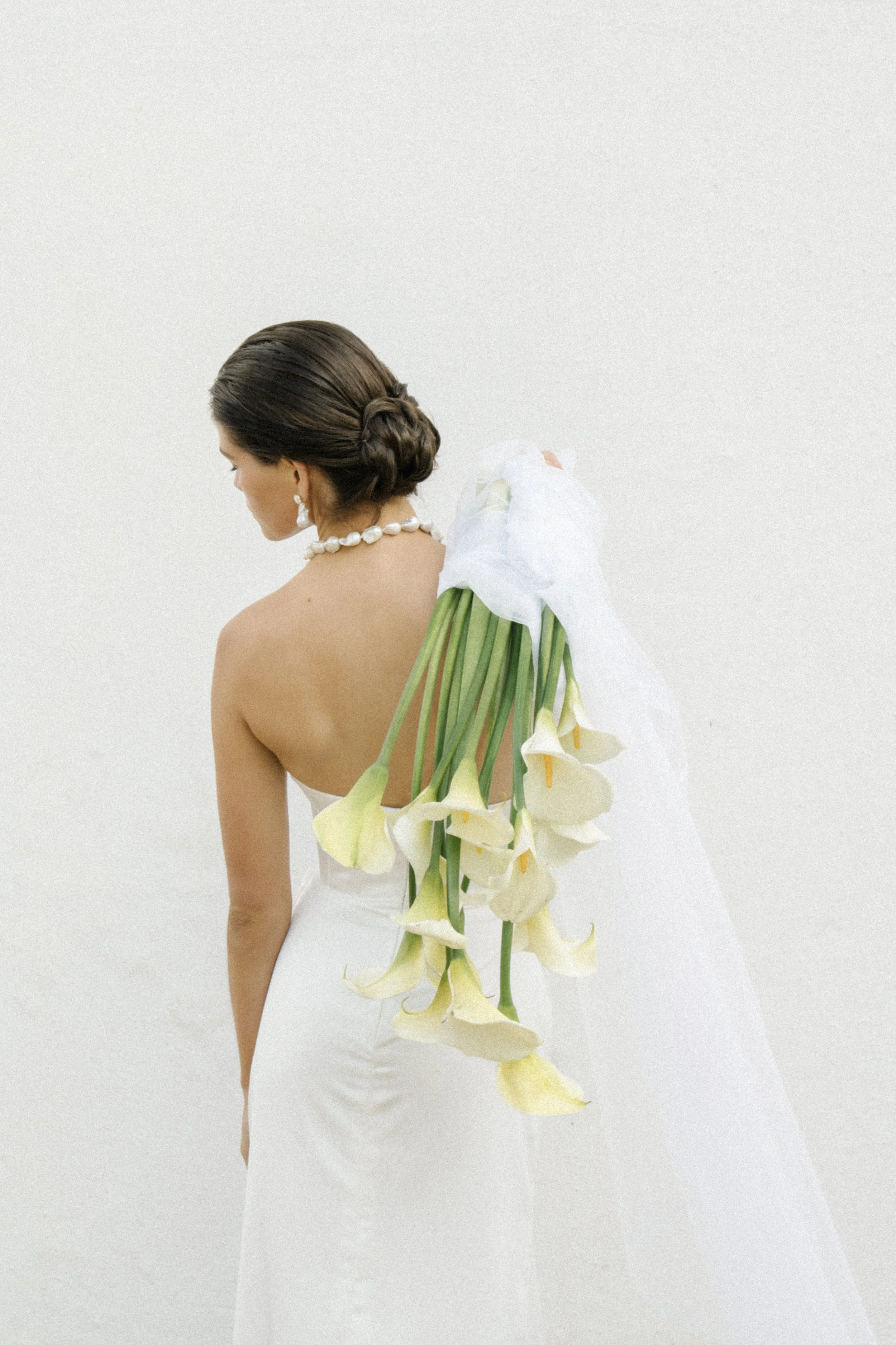 Bride in a white wedding dress holding a cascading bouquet of white calla lilies, viewed from behind.