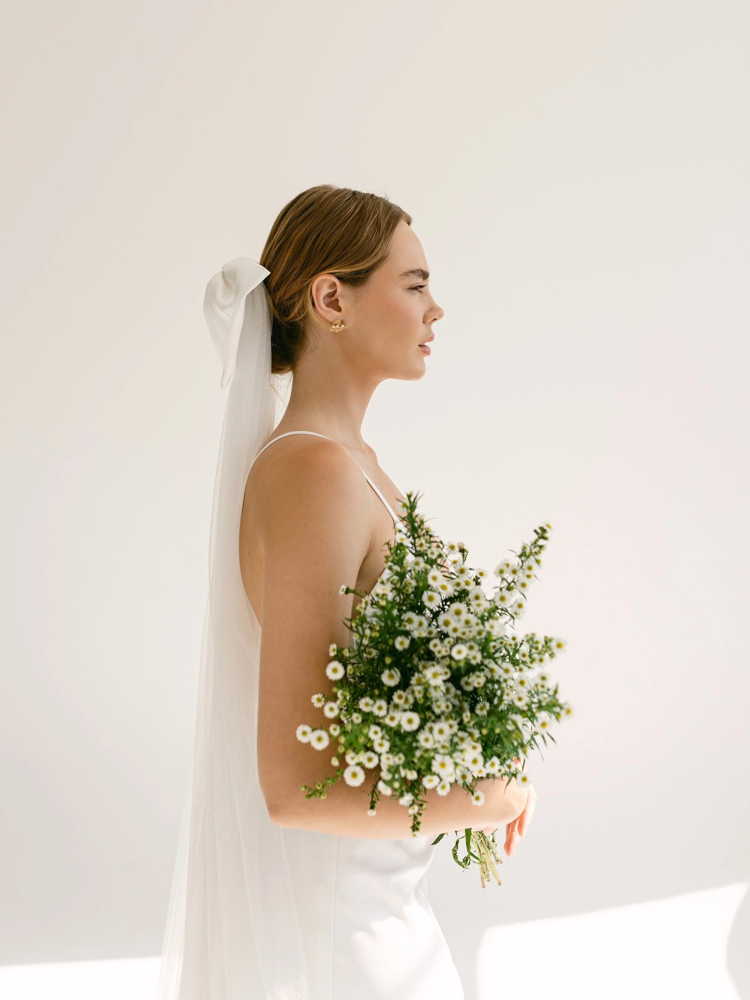 Bride in profile wearing a white veil and holding a bouquet of small white flowers