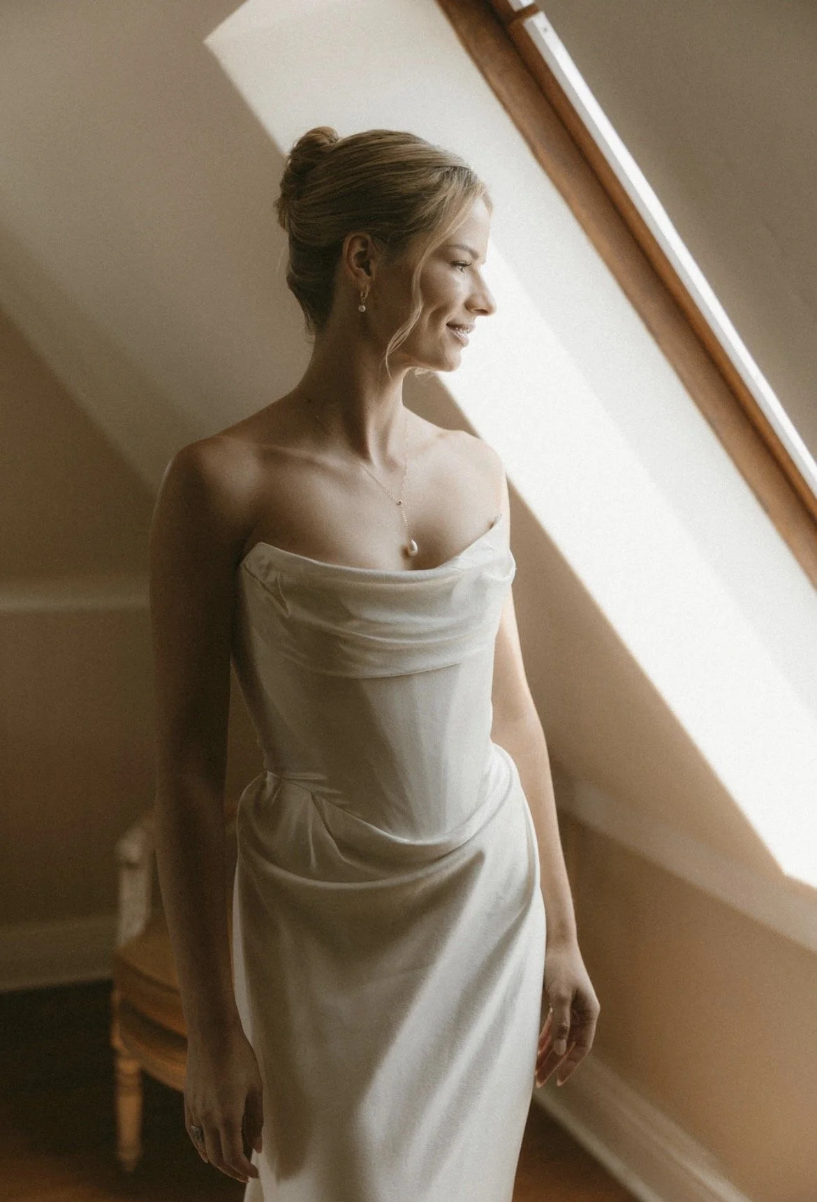 Bride in an elegant strapless white wedding dress standing by a sunlit window