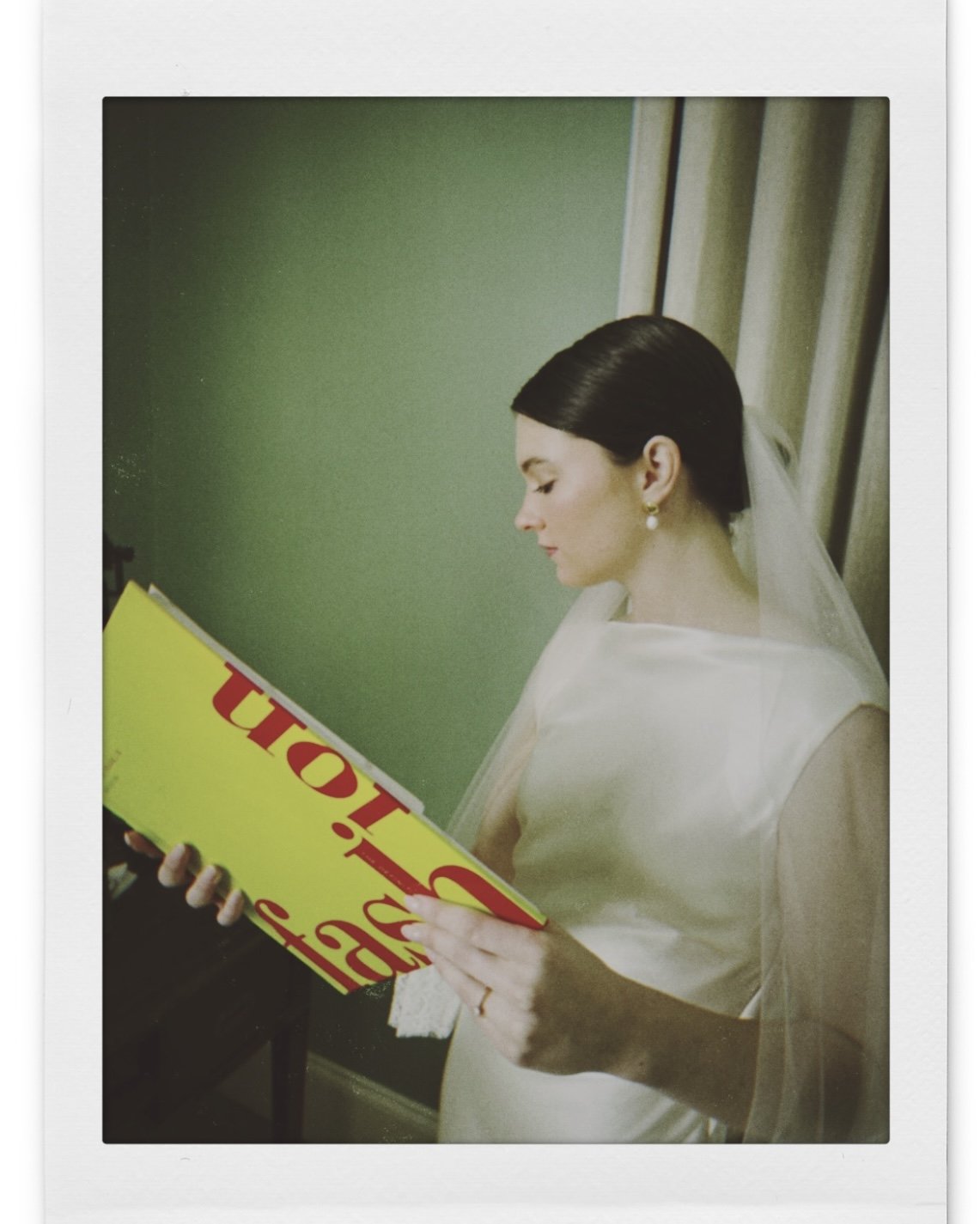 Bride in a white wedding dress and veil reading a large yellow book.