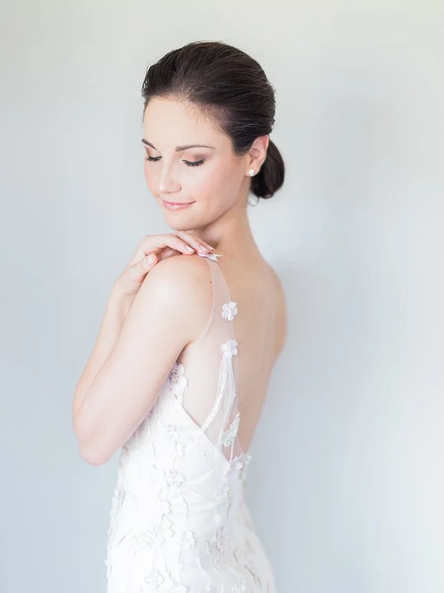 Bride wearing a white lace wedding dress with delicate straps, looking over her shoulder