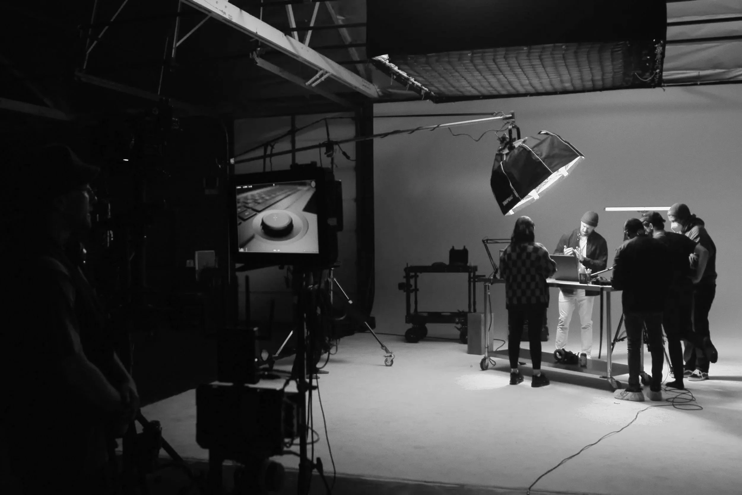 Black-and-white behind-the-scenes photo of a film crew shooting a scene in a studio with cameras, monitors, lighting equipment, and actors.