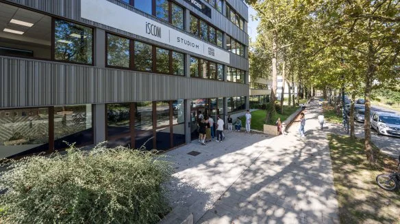 Façade moderne de l’ISCOM Studio à Paris, avec étudiants devant l’entrée et rue arborée attenante.