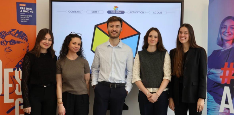 Cinq personnes posent devant un écran présentant une présentation « Big Idea », entourées de panneaux promotionnels colorés.