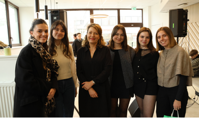 Groupe de six femmes souriantes posant ensemble dans un espace intérieur lumineux.