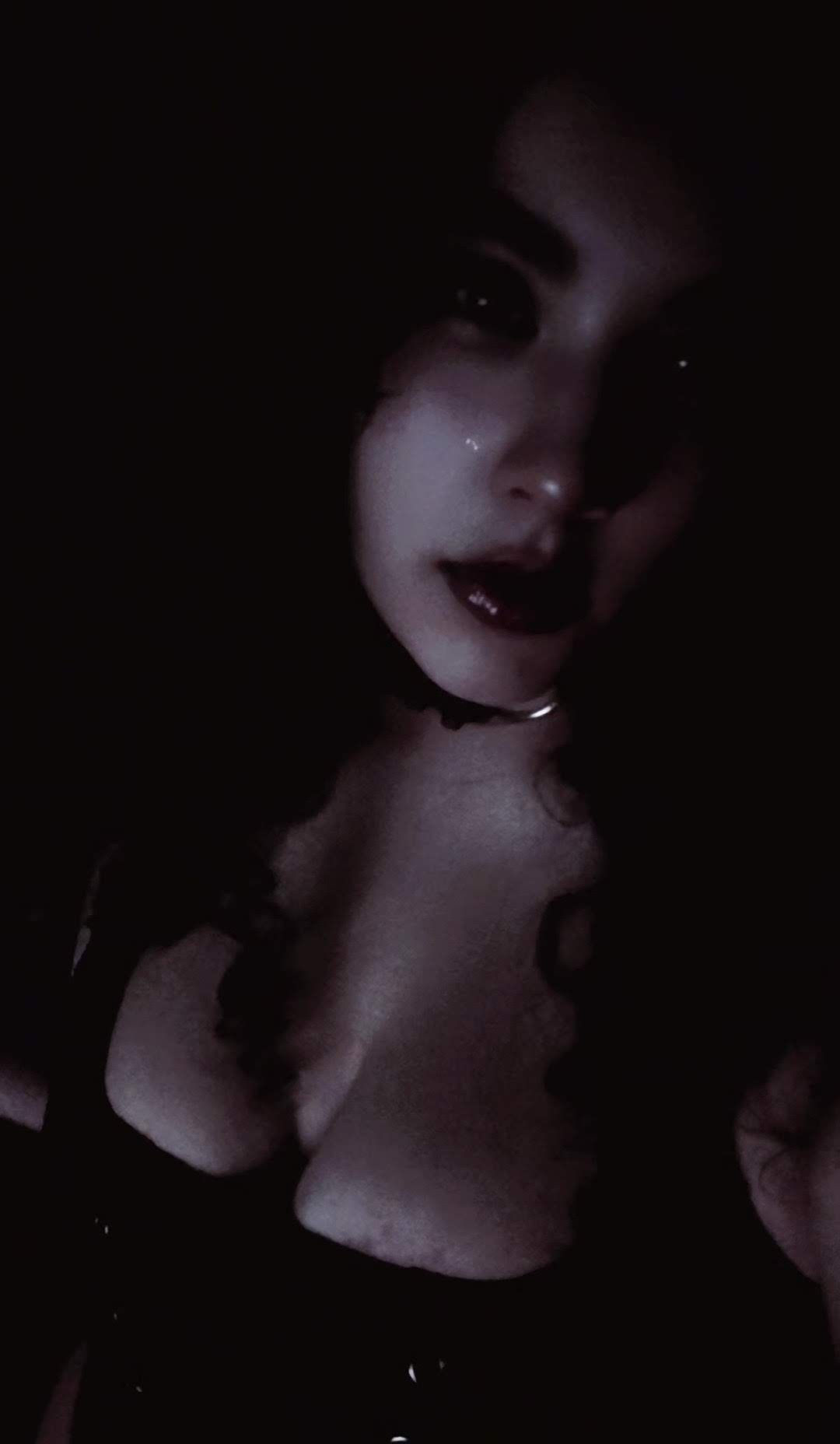 Close-up portrait of a person with dark hair and lipstick wearing a black choker in dim lighting