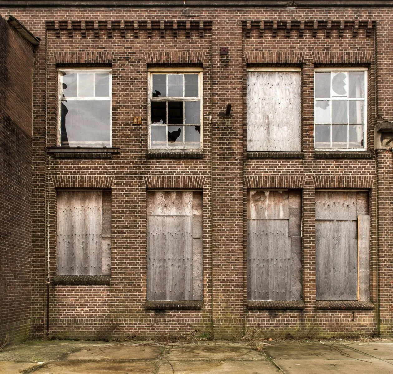 Abandoned brick rowhome before renovation — boarded-up windows and a neglected facade