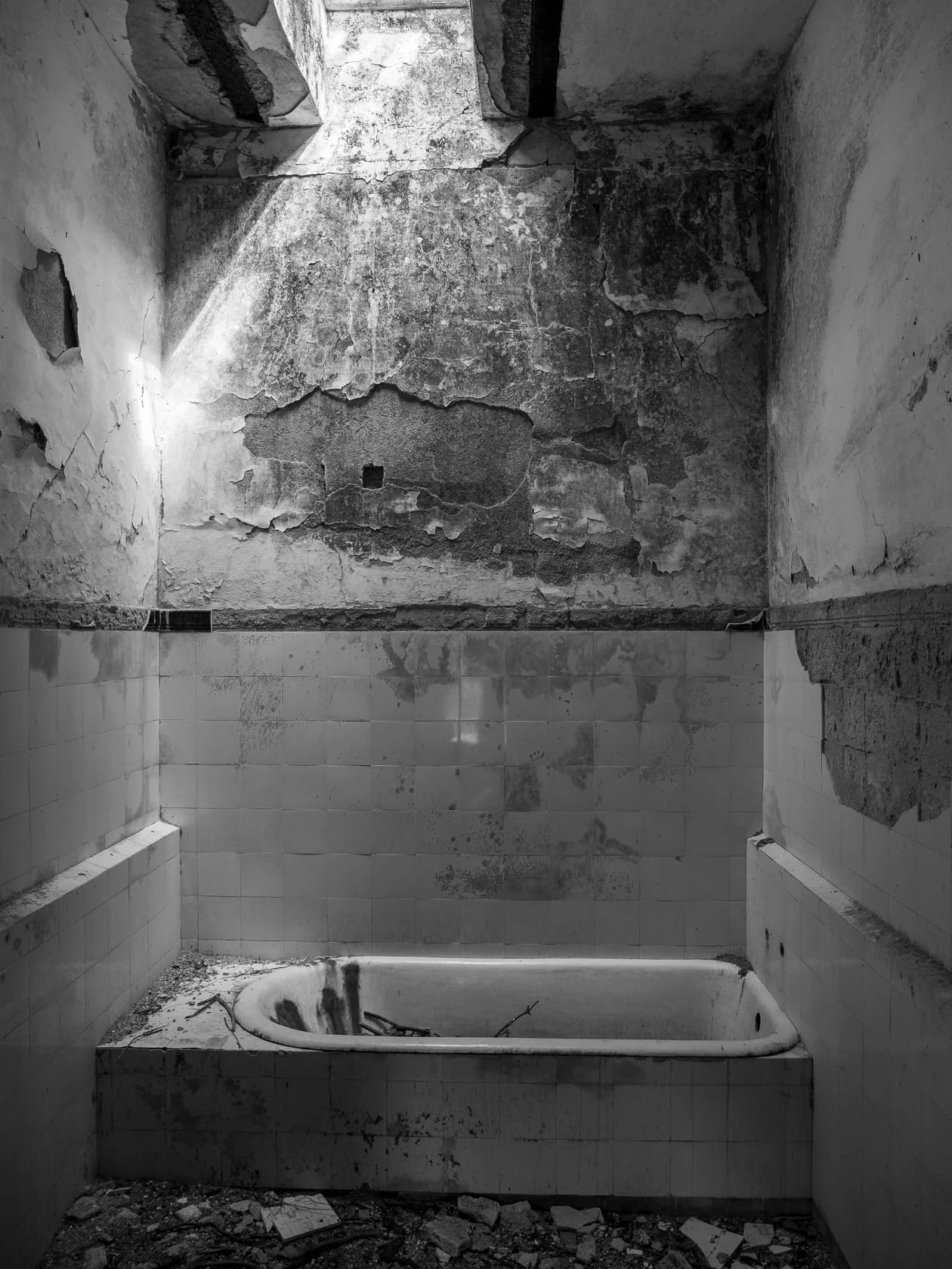 Derelict bathroom before renovation — a stained tub and crumbling tile, photographed in black and white