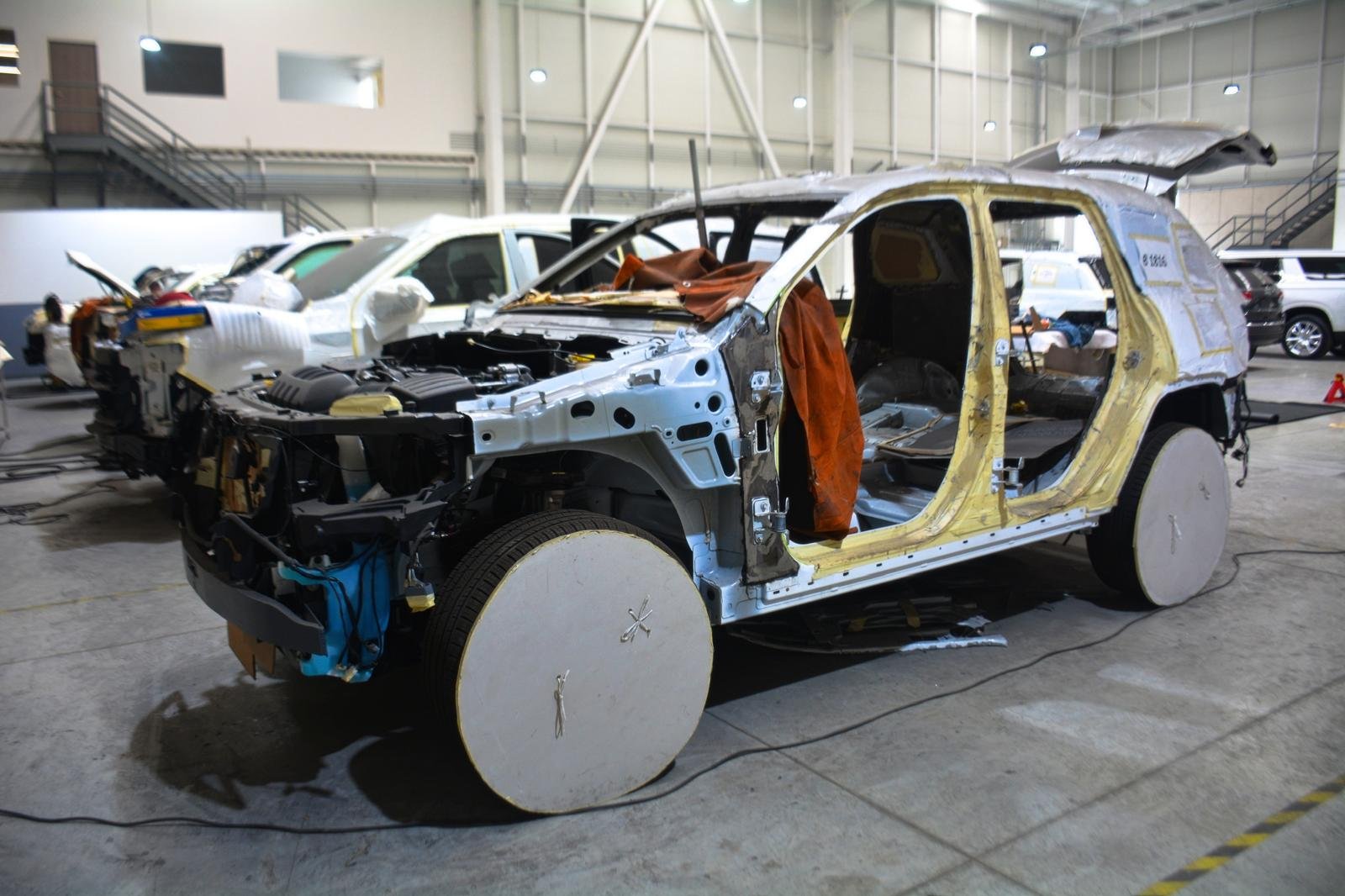 Prototipo de automóvil eléctrico desmontado en un taller industrial, con carrocería expuesta, bolsas de aire y ruedas cubiertas.