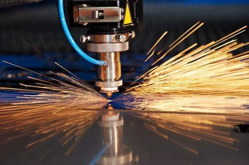 Cortadora láser industrial cortando una lámina de metal y produciendo chispas.