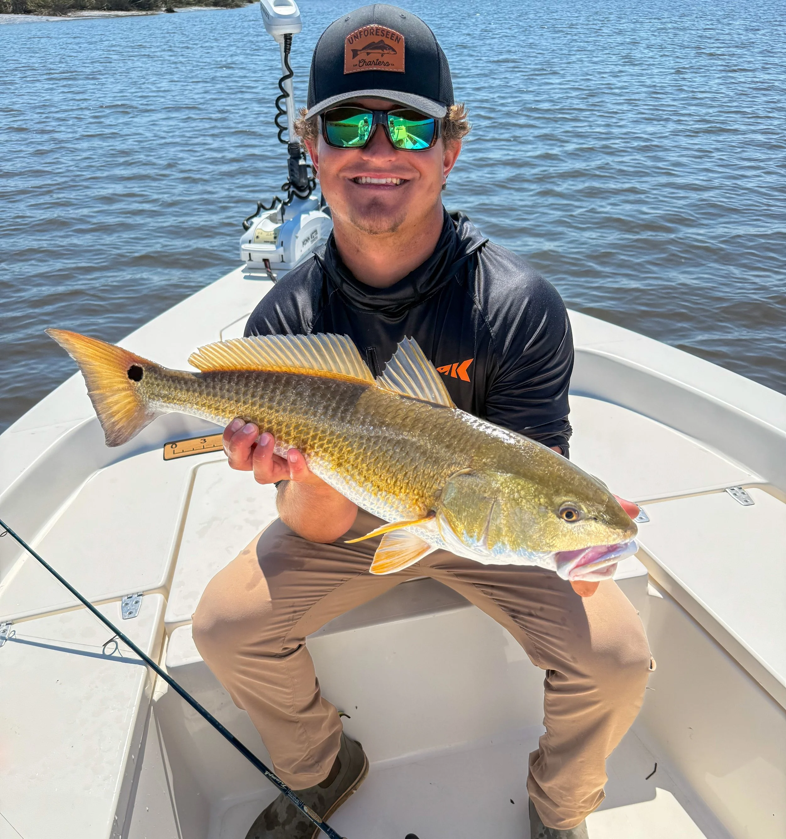 Smiling angler holding a large redfish on a boat over coastal waters