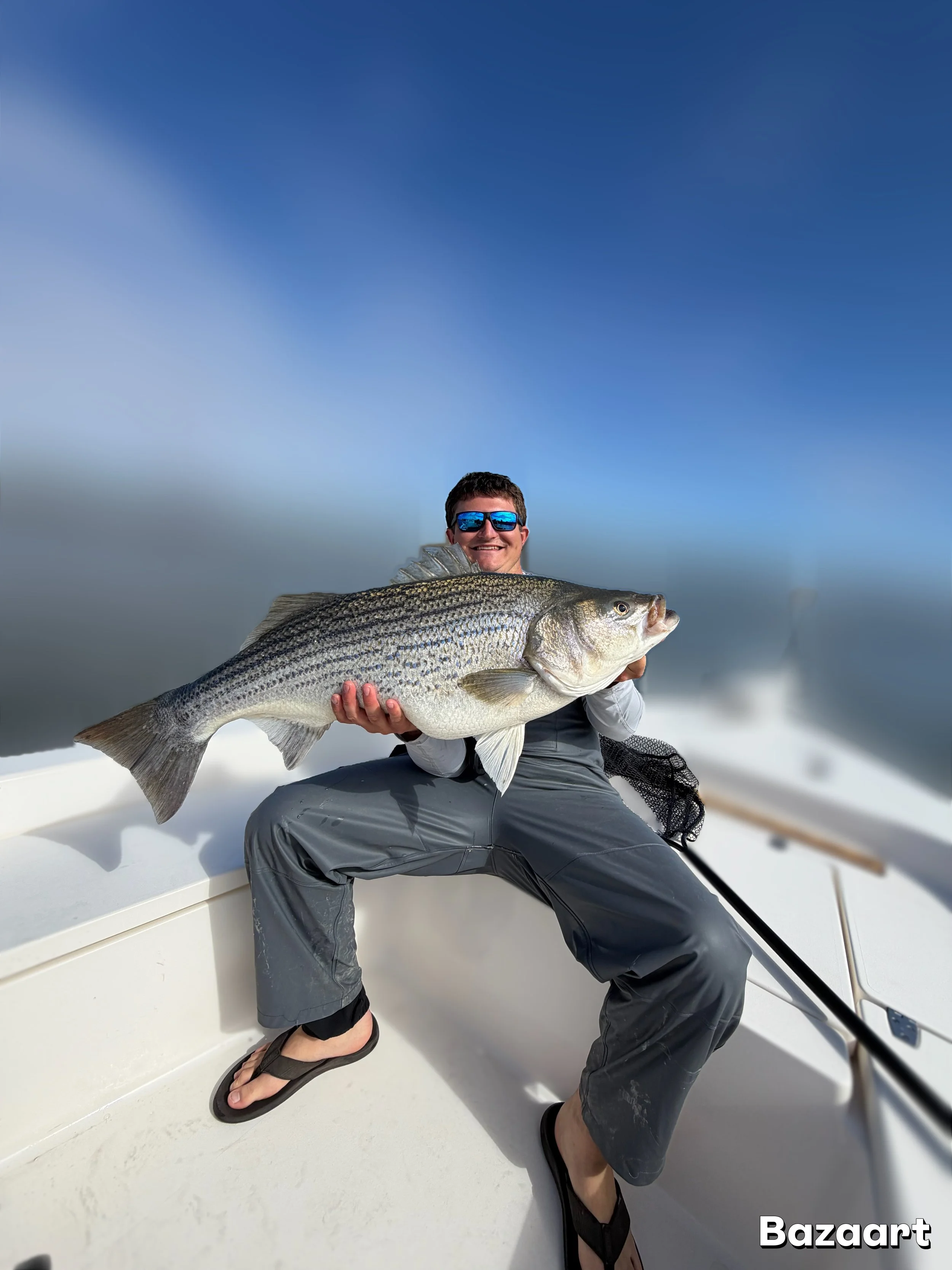 Angler wearing sunglasses holds a large striped fish on a boat.
