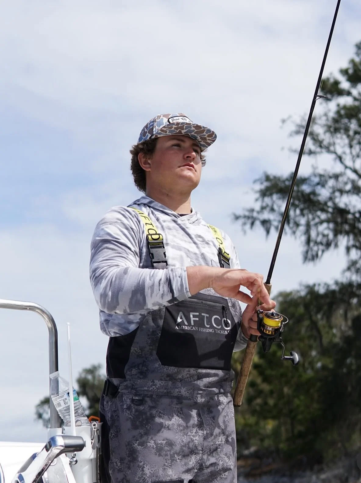 Angler in camouflage fishing gear holding a spinning rod on a boat