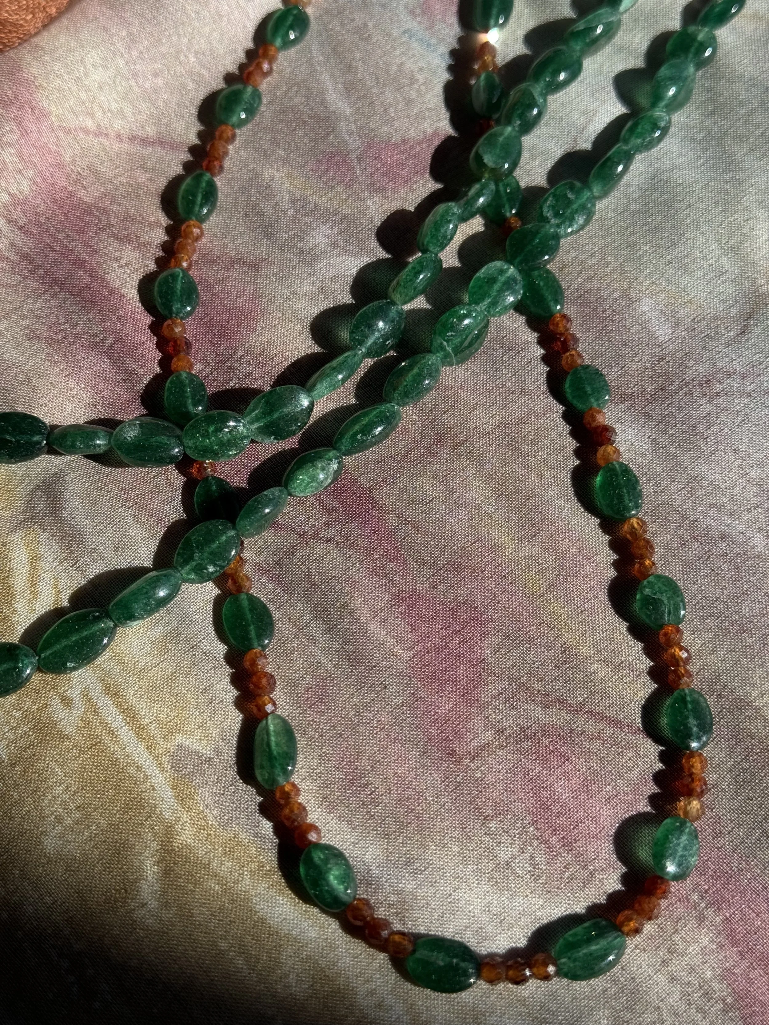 Close-up of green and amber beaded necklaces arranged on patterned fabric.