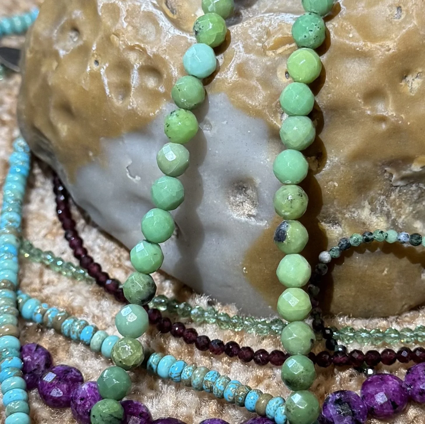 Close-up of colorful faceted gemstone bead necklaces arranged on a tan stone surface