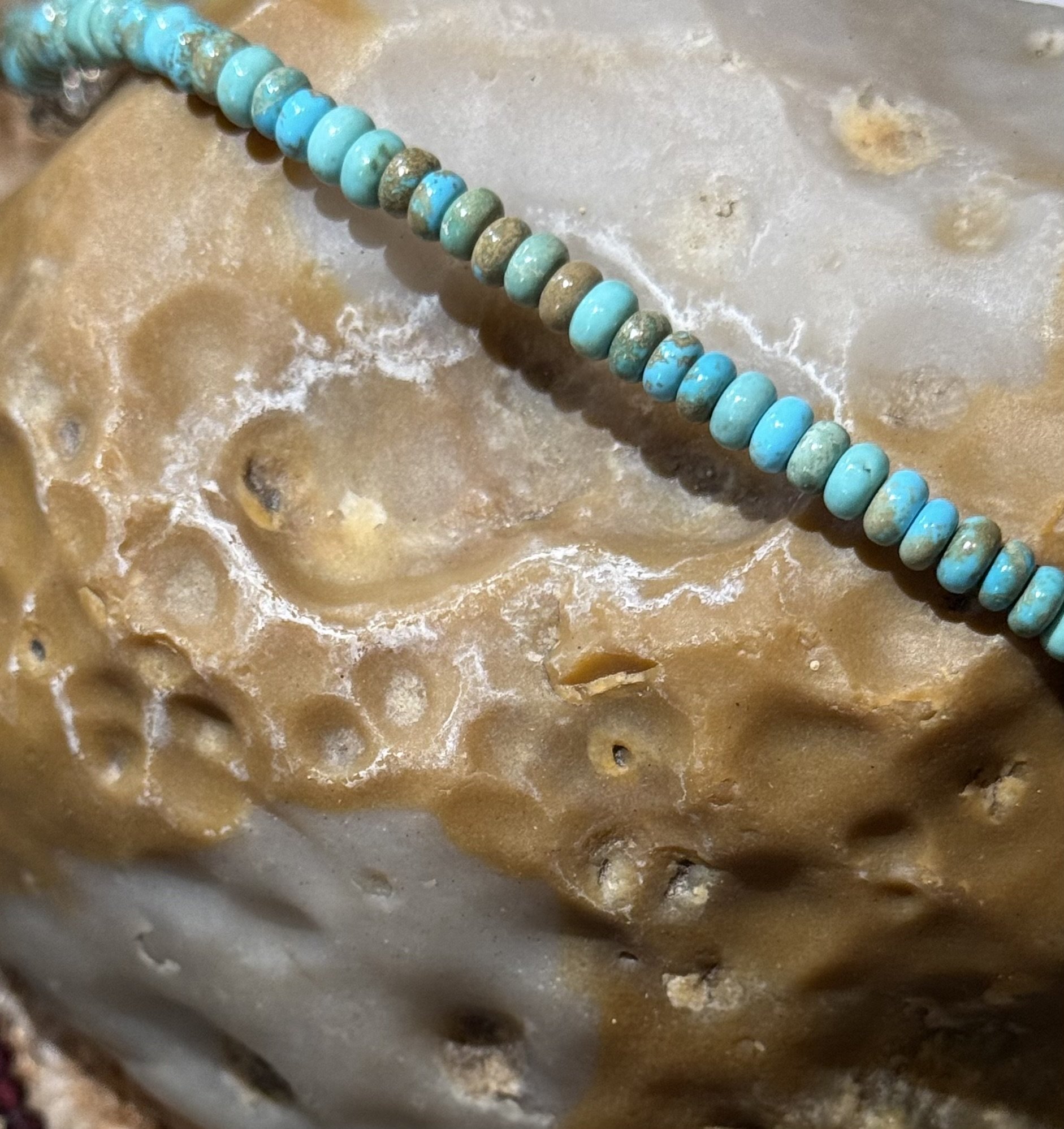 Close-up of turquoise and brown stone beads on a textured natural stone surface