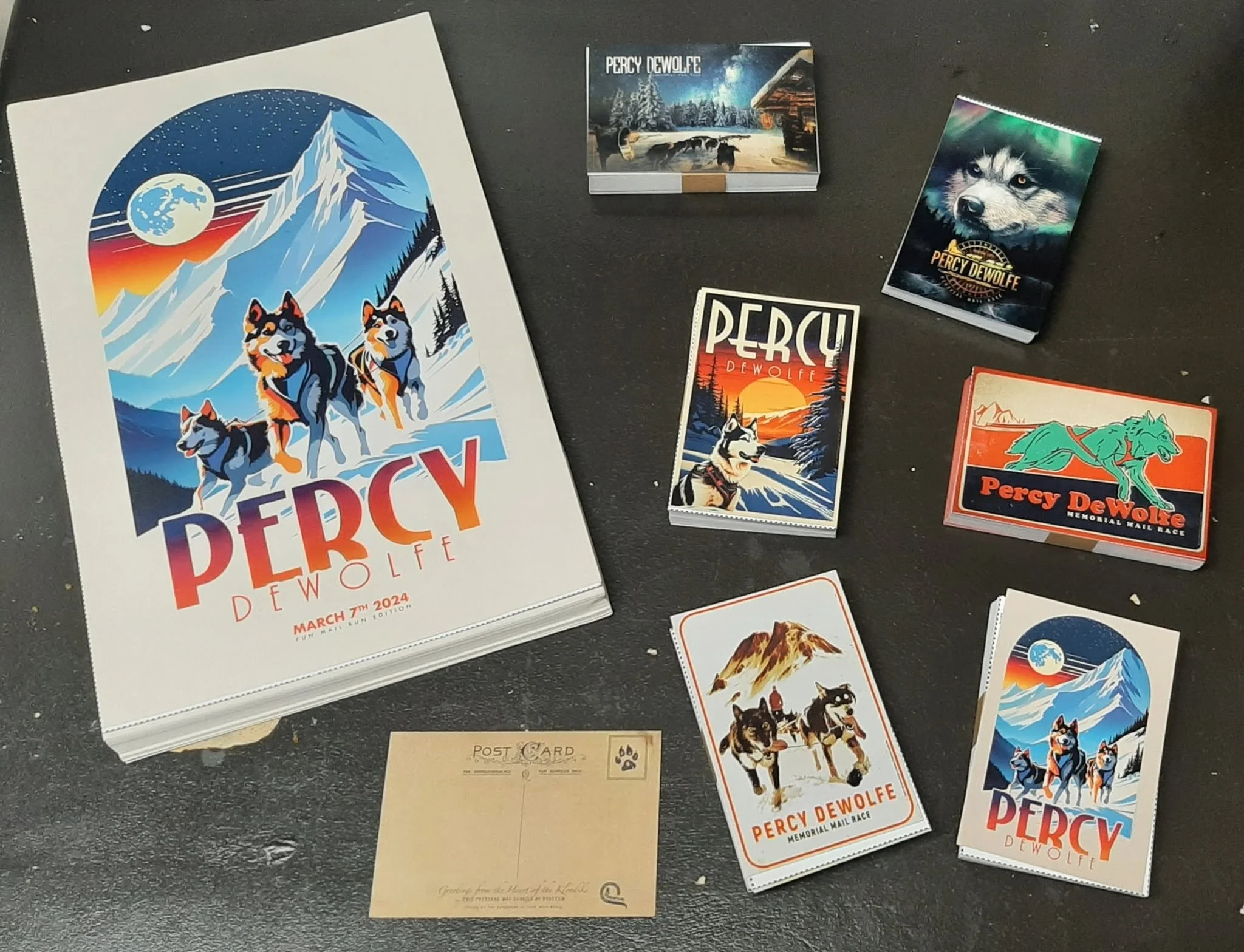 Percy DeWolfe Memorial Mail Race posters, postcards, and souvenir cards featuring sled dogs in snowy mountain landscapes.