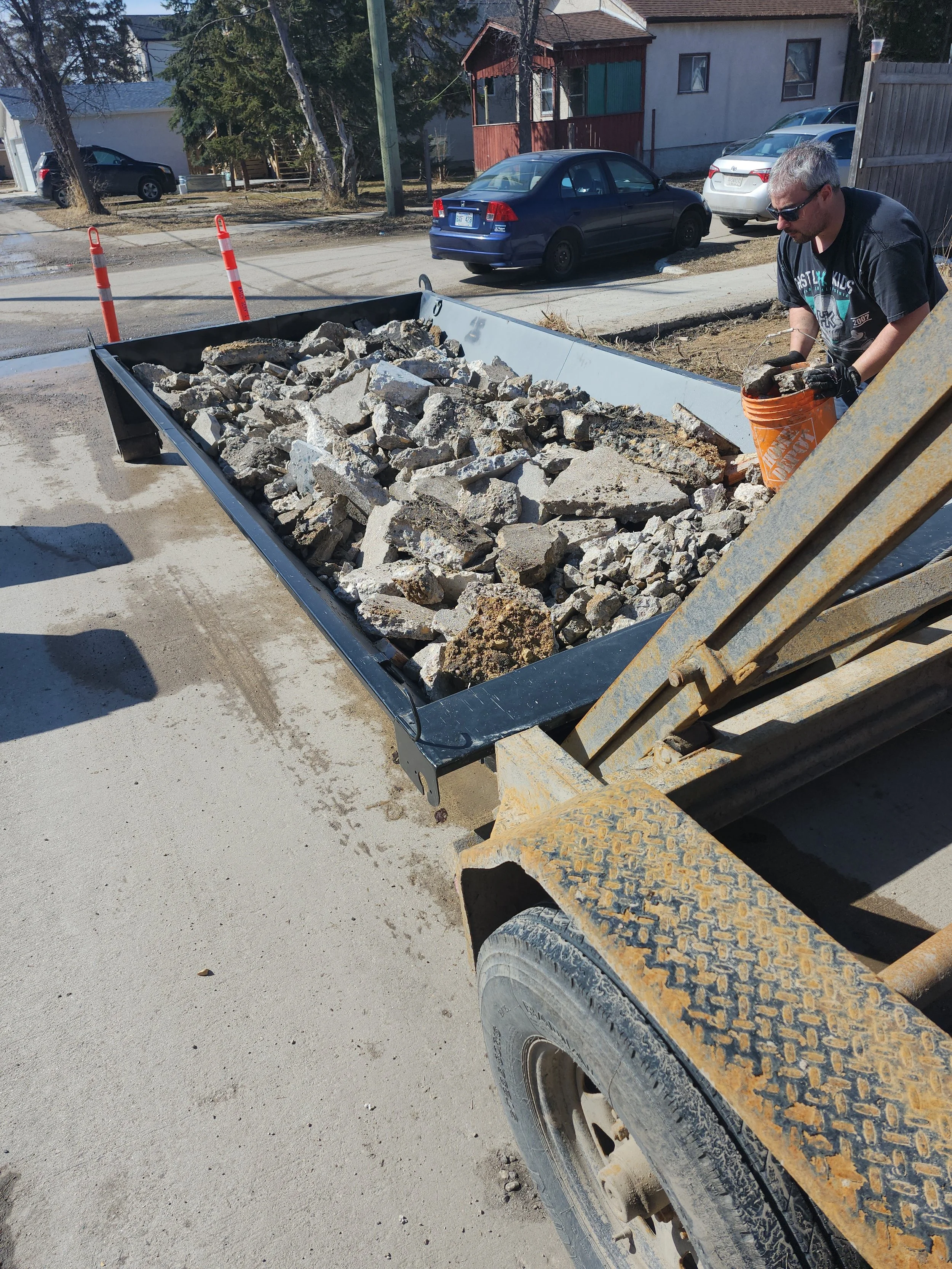 Construction worker loading broken concrete into a front-end loader bucket on a residential street.