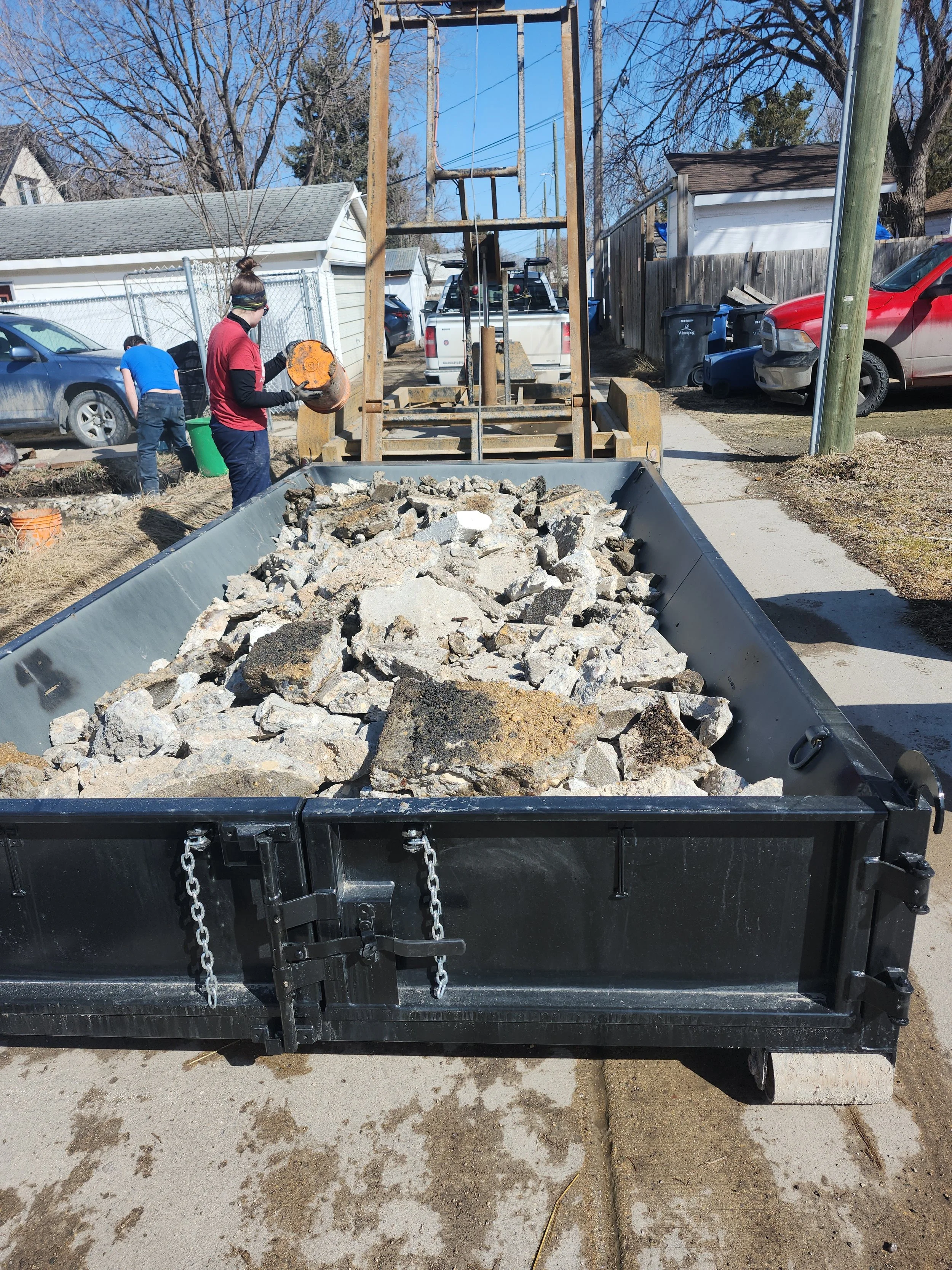 Workers load broken concrete into a debris trailer during residential construction cleanup.