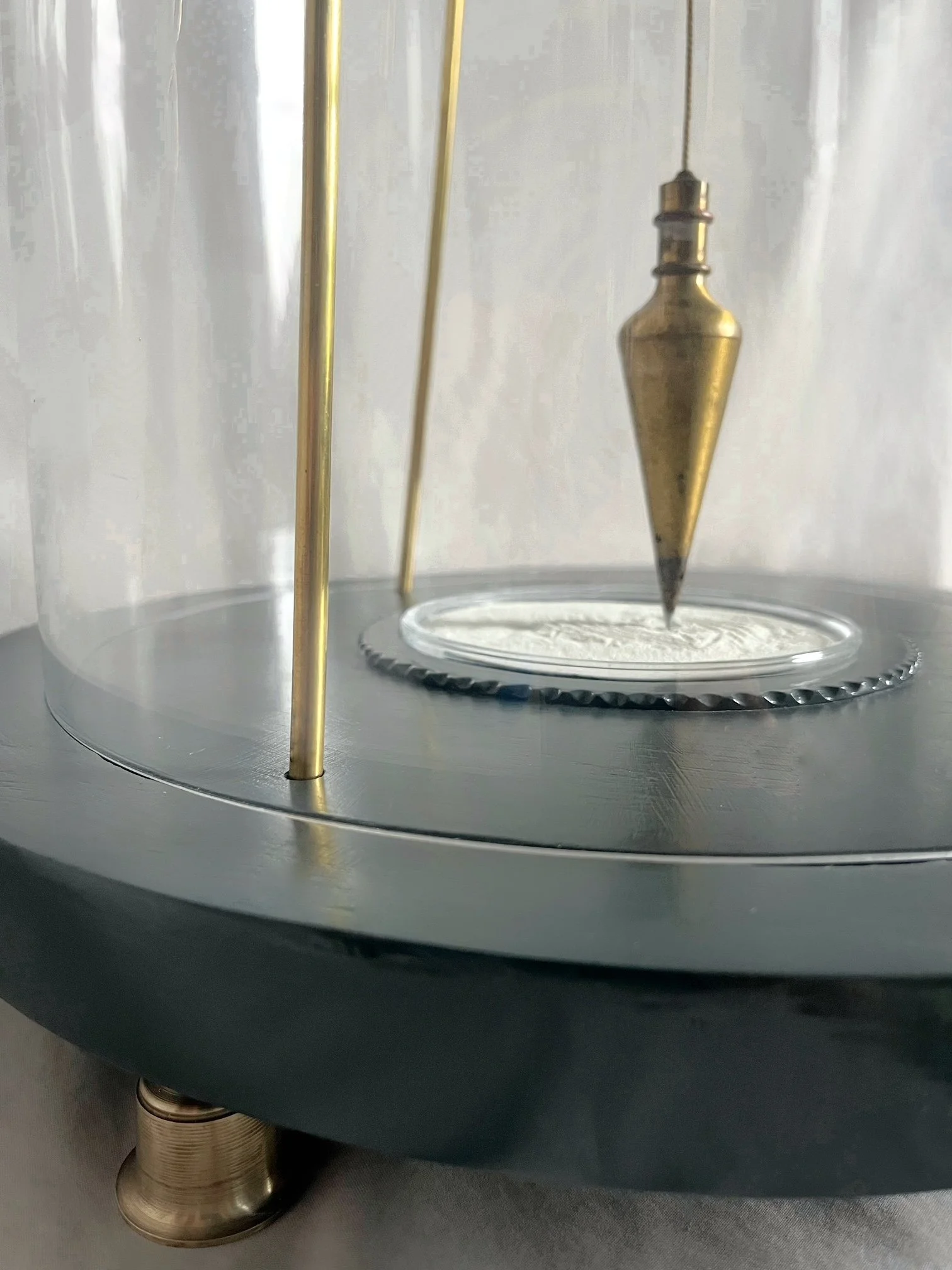 Close-up of a brass pendulum suspended inside a glass-domed clock over a silver clock face.