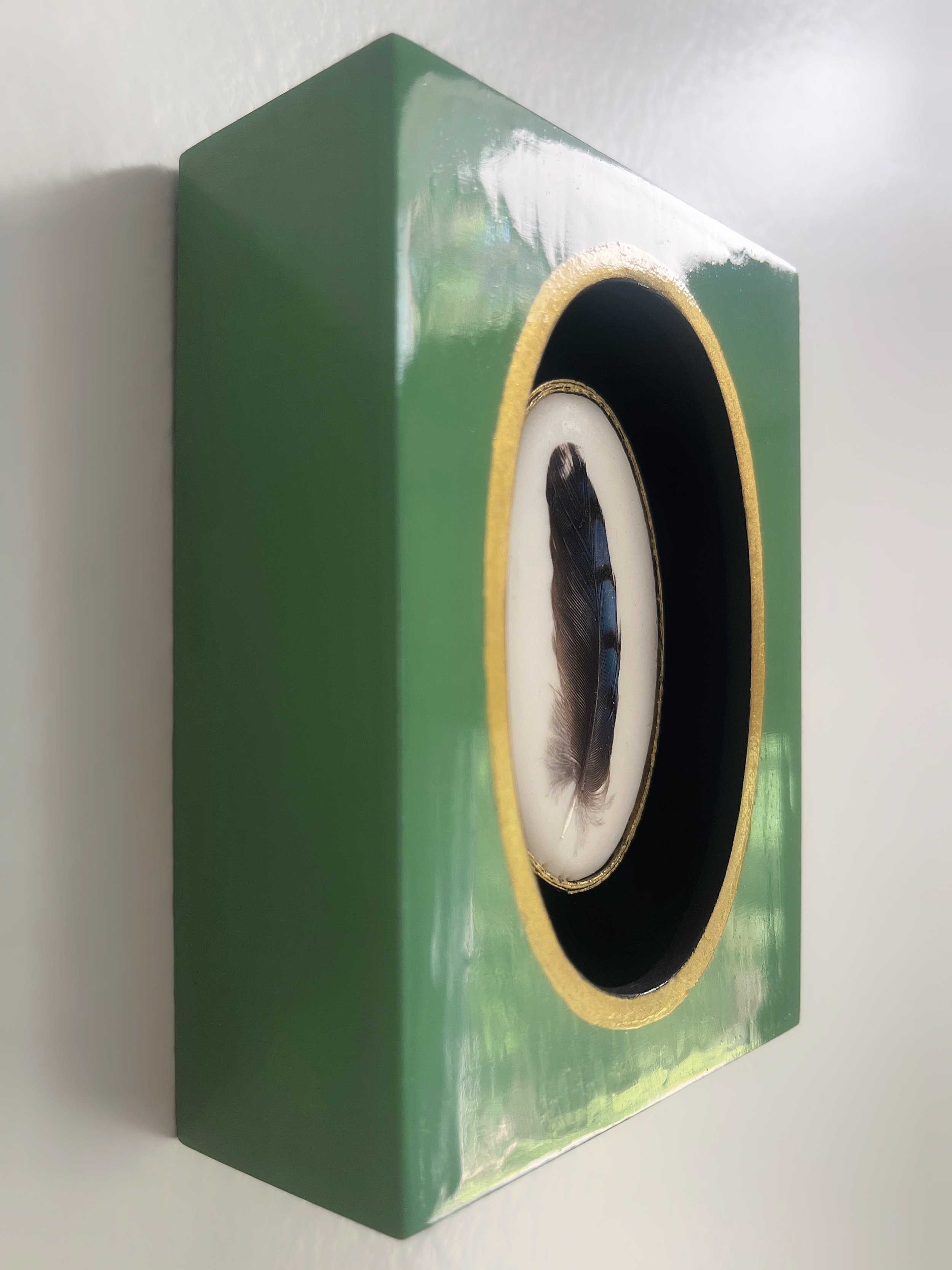 Close-up of a green wooden birdhouse with a gold-trimmed entrance and feather inside