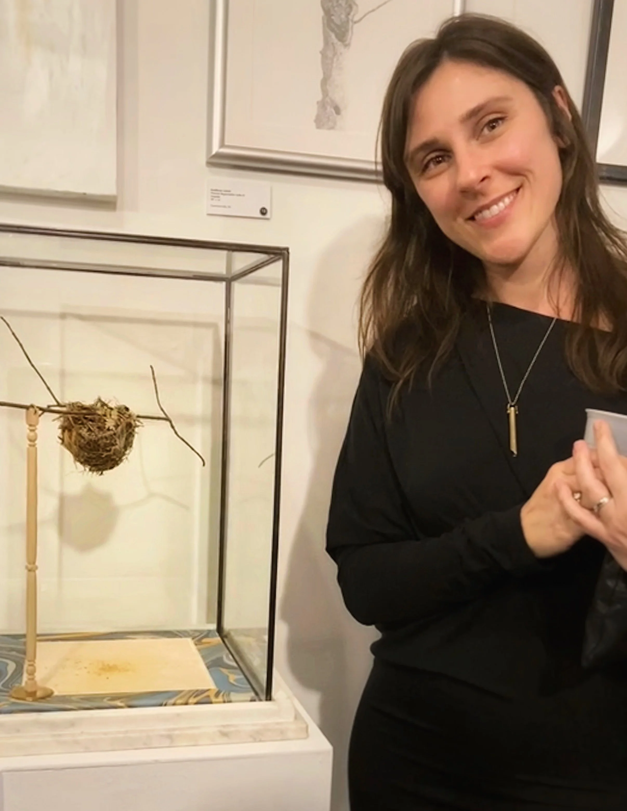 Smiling woman in black standing beside a framed butterfly display and artwork