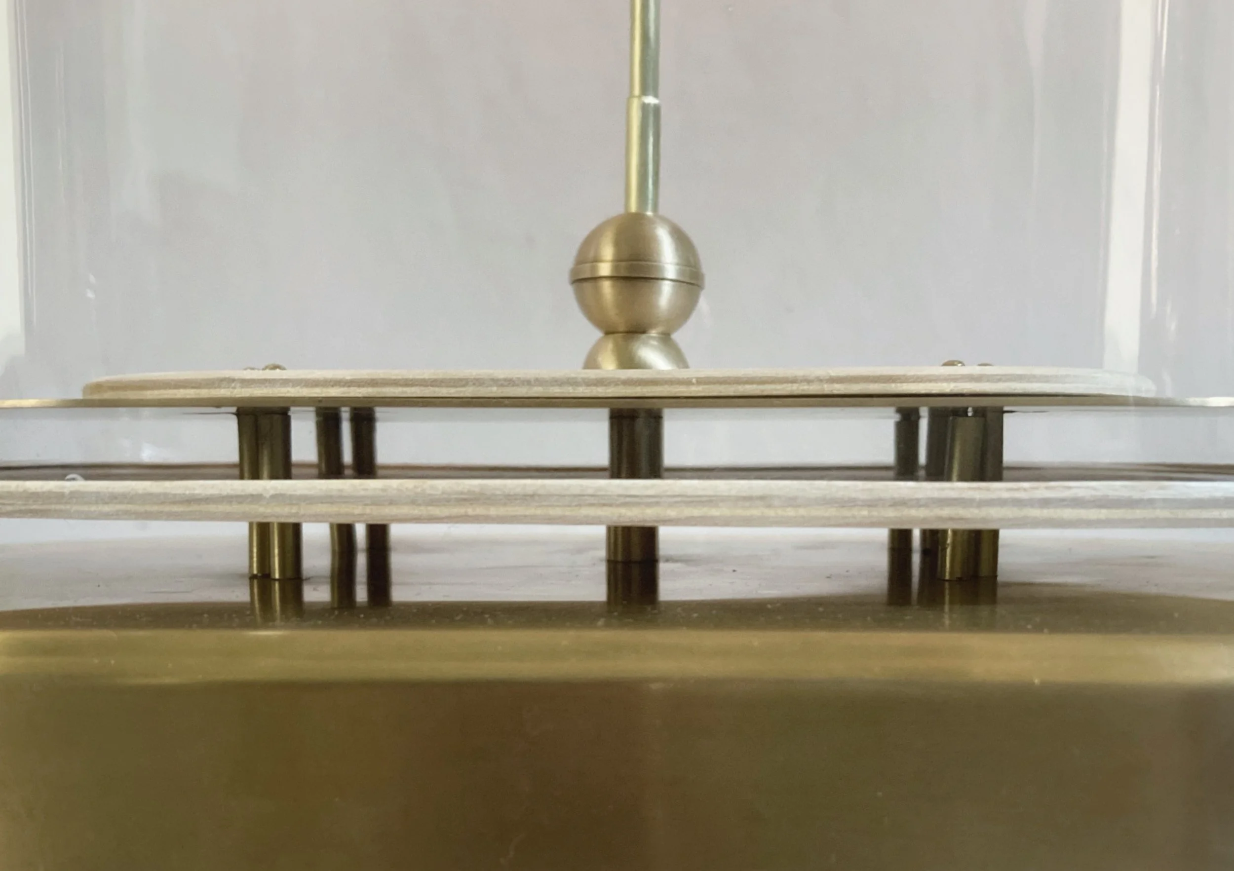 Close-up of a brass mechanical assembly with spherical weights, rods, and horizontal wooden rails behind glass