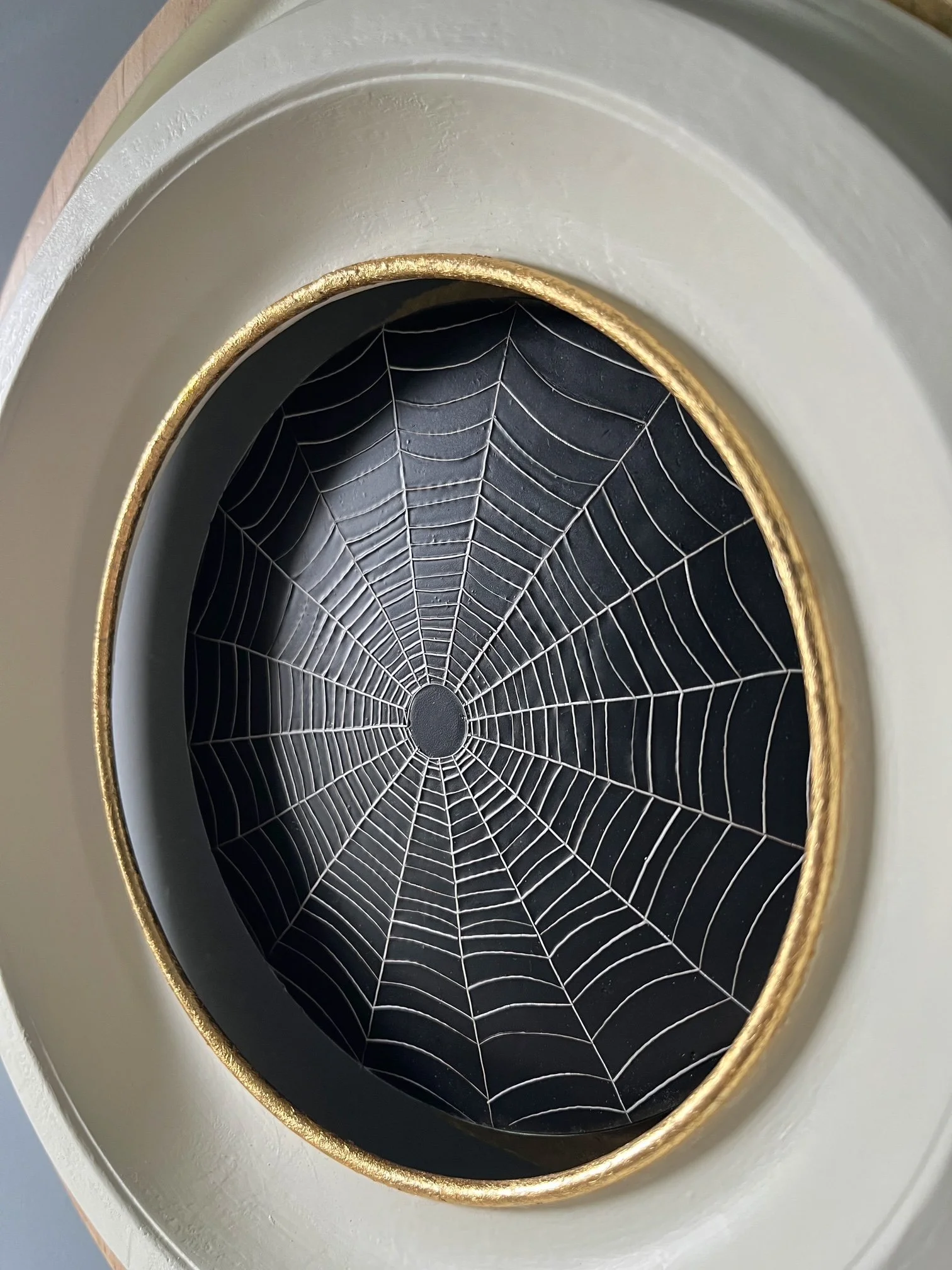 Close-up of a black spiderweb design with a gold-trimmed oval frame.