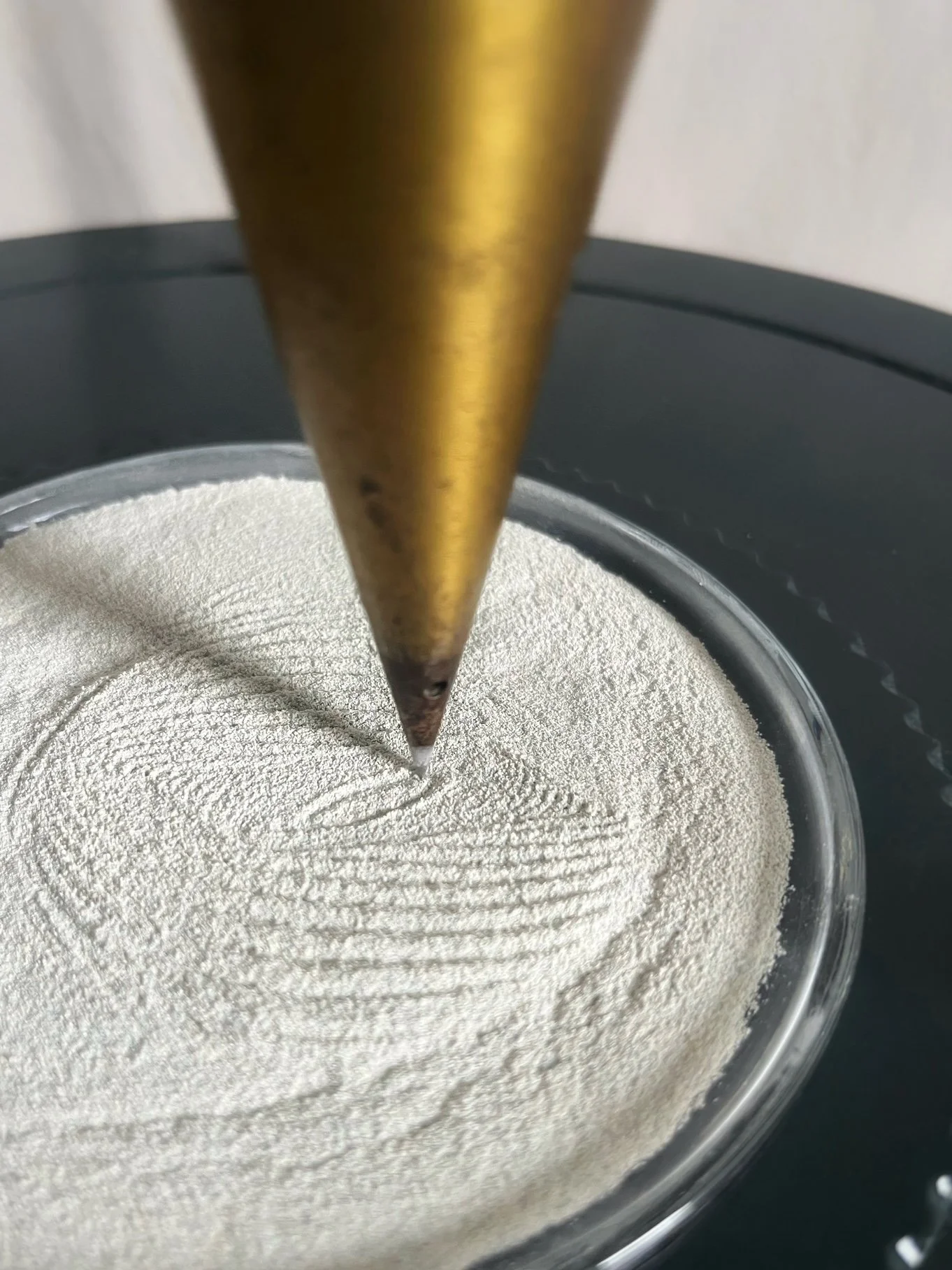 Close-up of a pointed wooden tool pressing into fine white powder in a glass dish