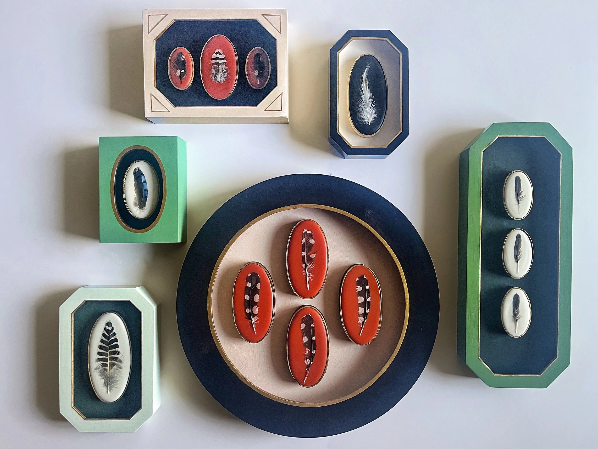 Decorative framed feather artwork arranged around a central circular display in navy, coral, mint green, and gold