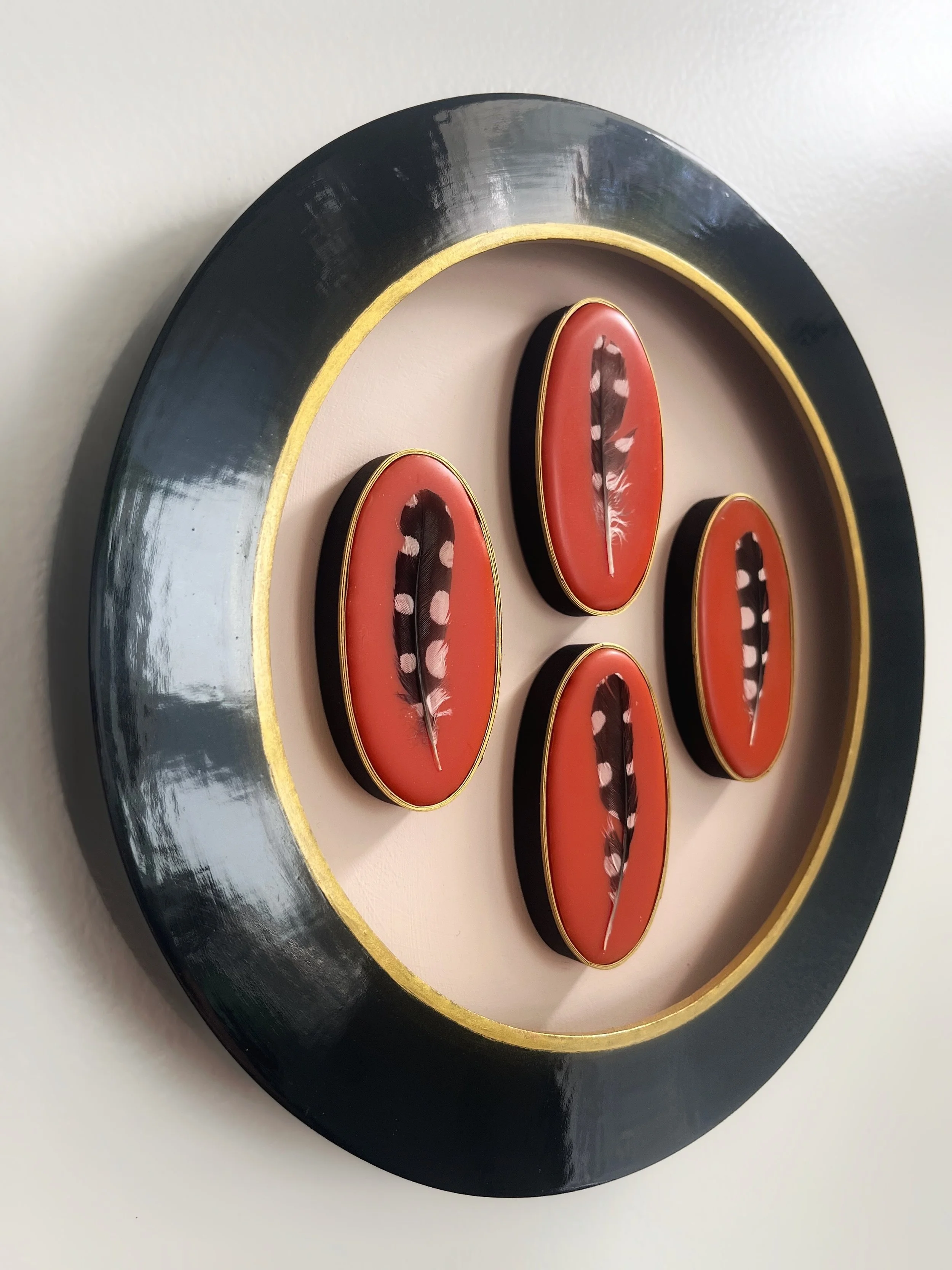 Black decorative plate with gold trim and red oval accents featuring feather designs