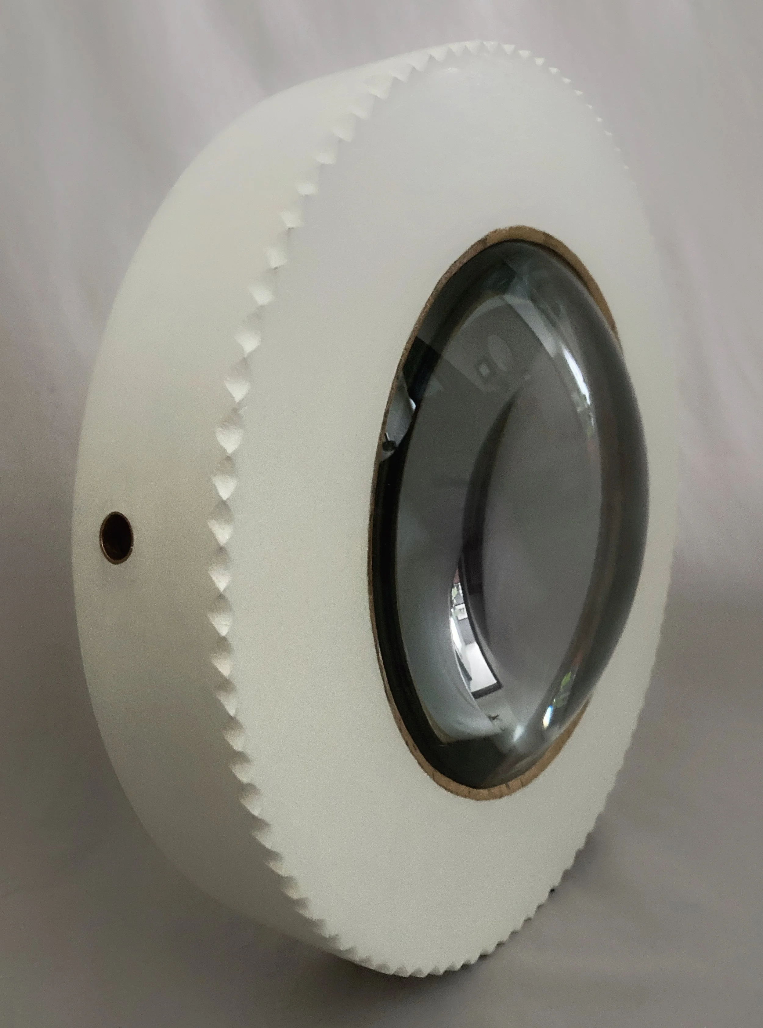 Close-up of a white circular device with a dark oval opening and scalloped edge on a gray surface.