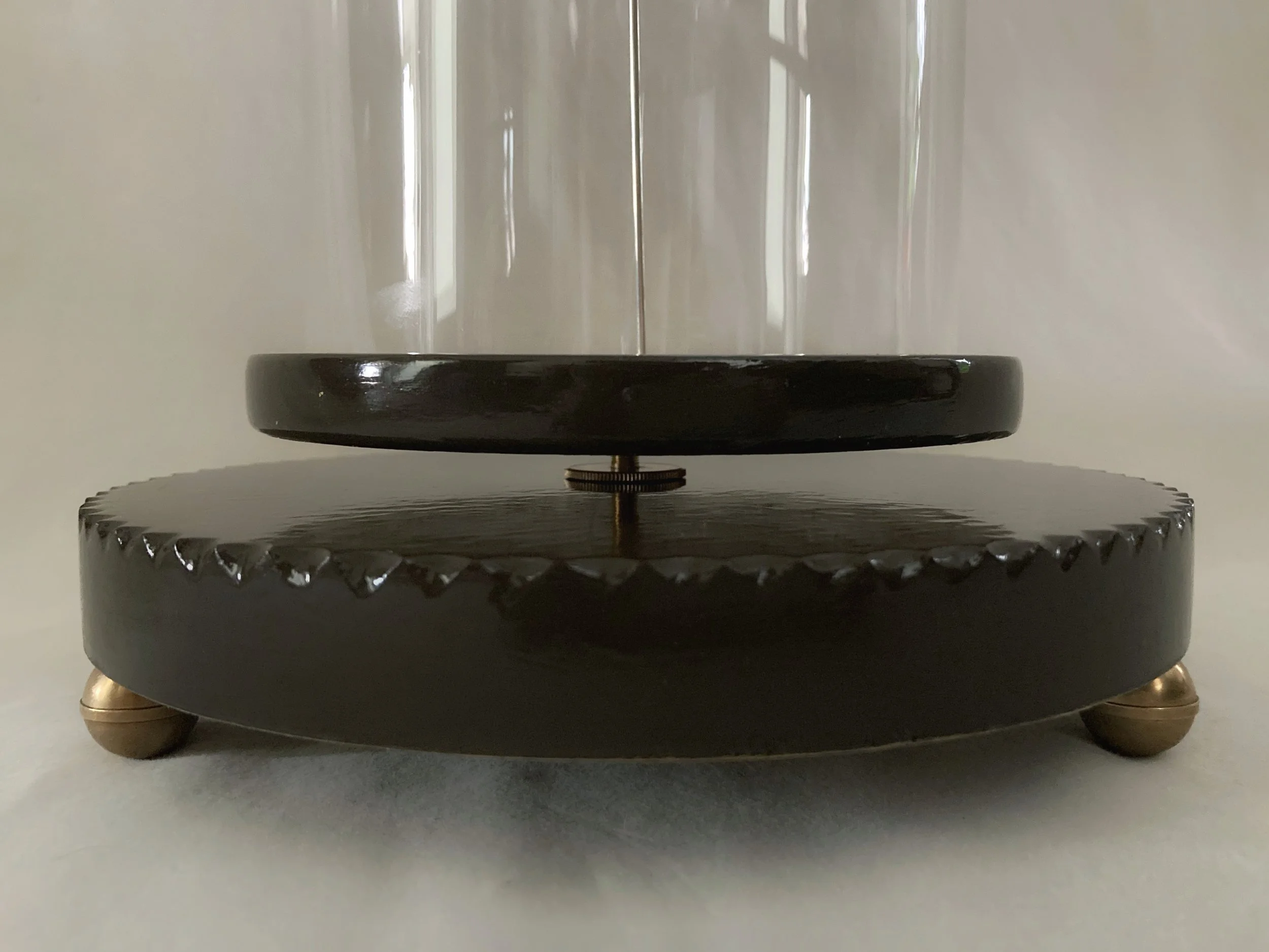 Close-up of a black turntable with a clear glass platter, decorative edge, and brass feet.