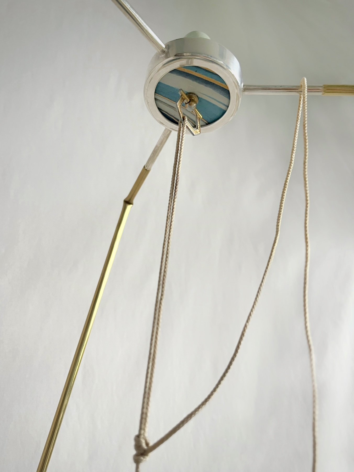 Close-up of a decorative ceiling light fixture with a marbled blue-and-white glass canopy, brass rods, and hanging pull cords