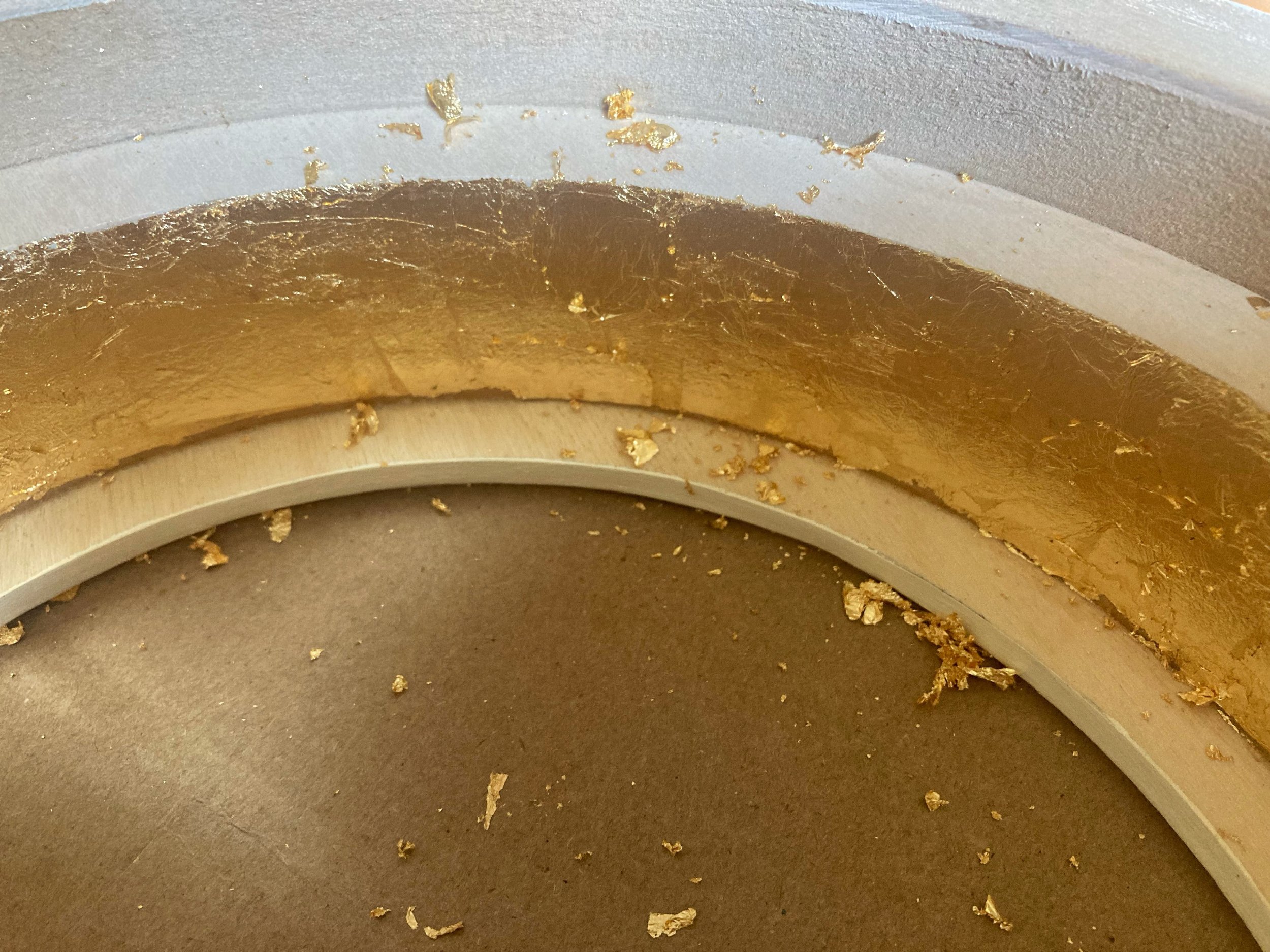 Close-up of gold leaf flakes and residue on a curved metallic surface