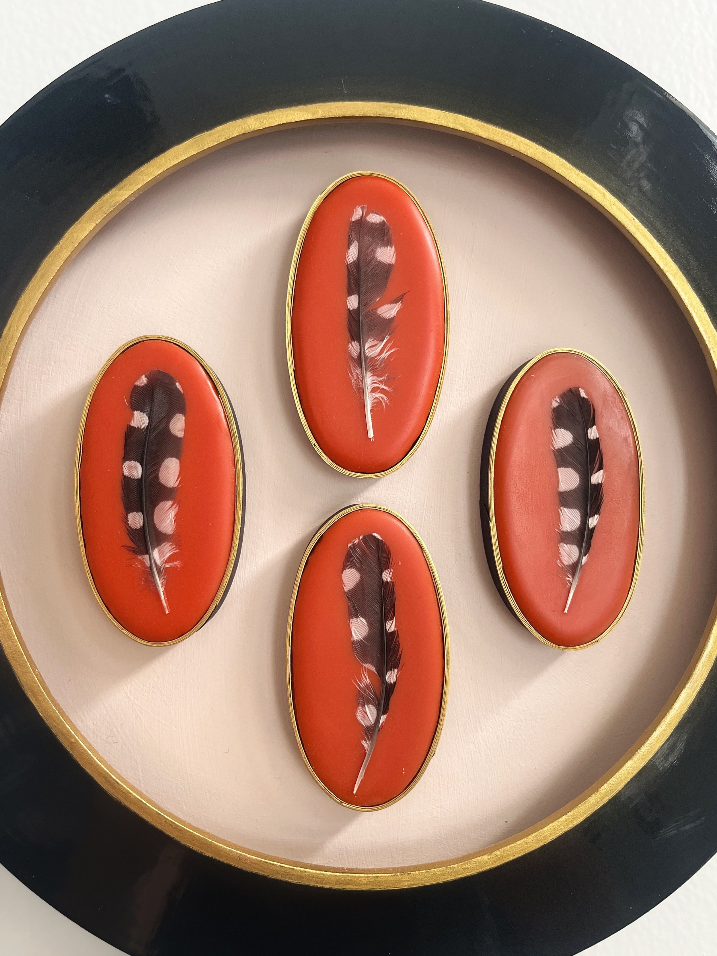 Close-up of four red oval decorative plaques with gold trim and bird feathers, arranged in a black circular frame.